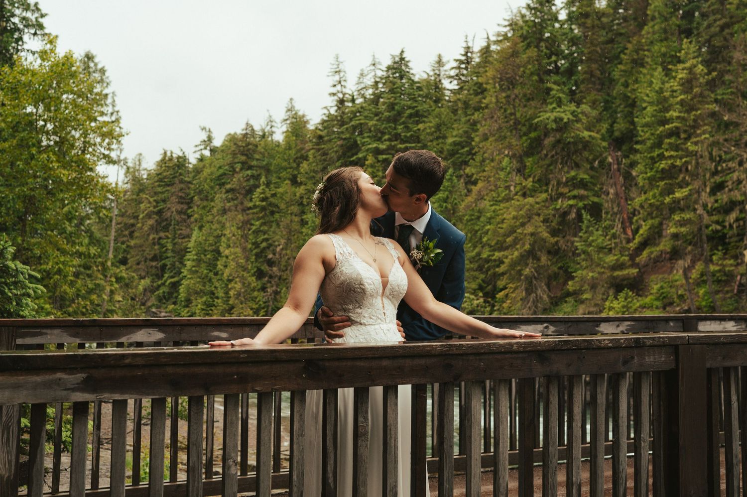 Wedding party gathered on wooden deck surrounded by evergreen forest scenery.