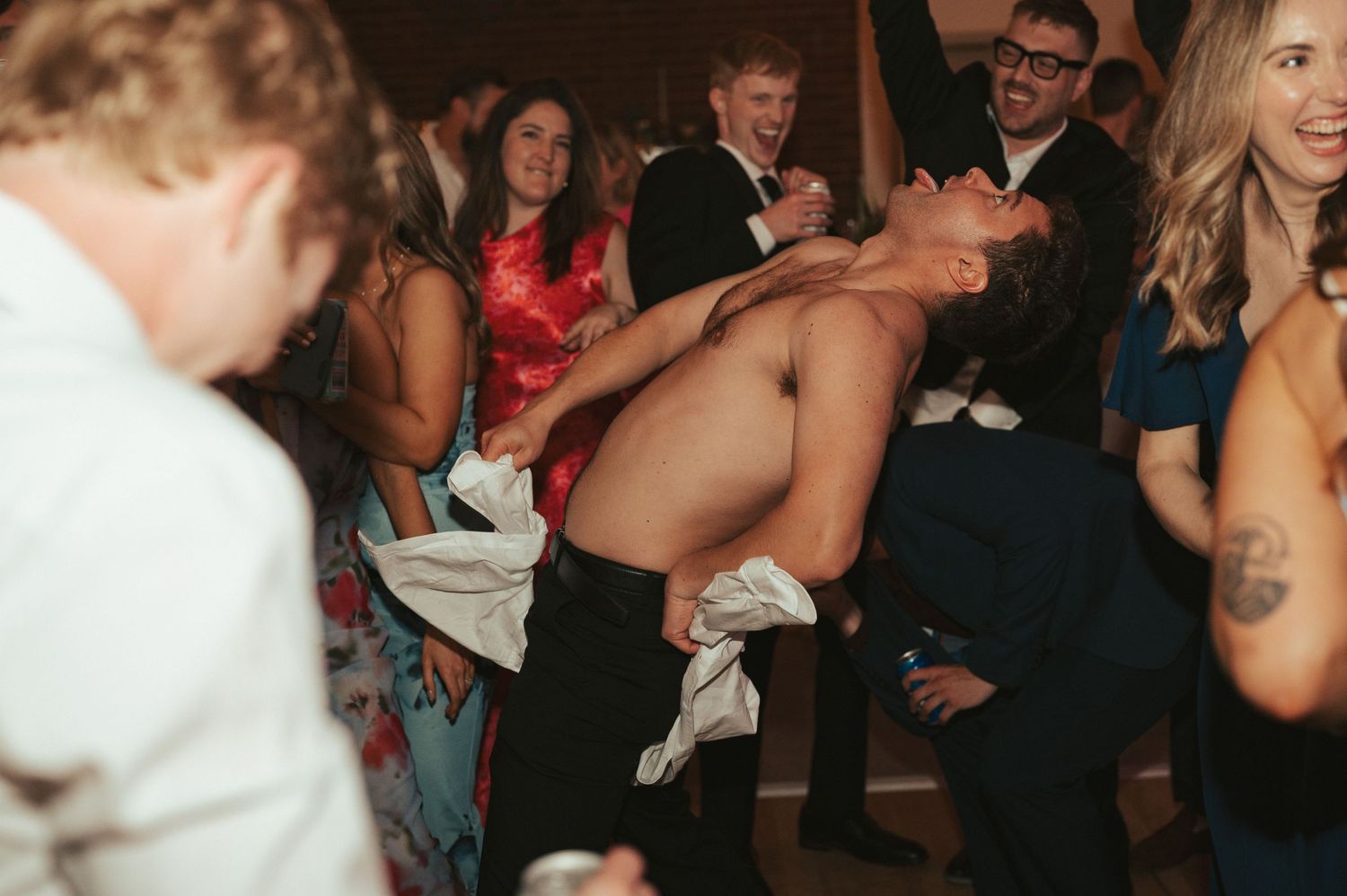 Wedding reception guests dance and celebrate on a dimly lit dance floor.