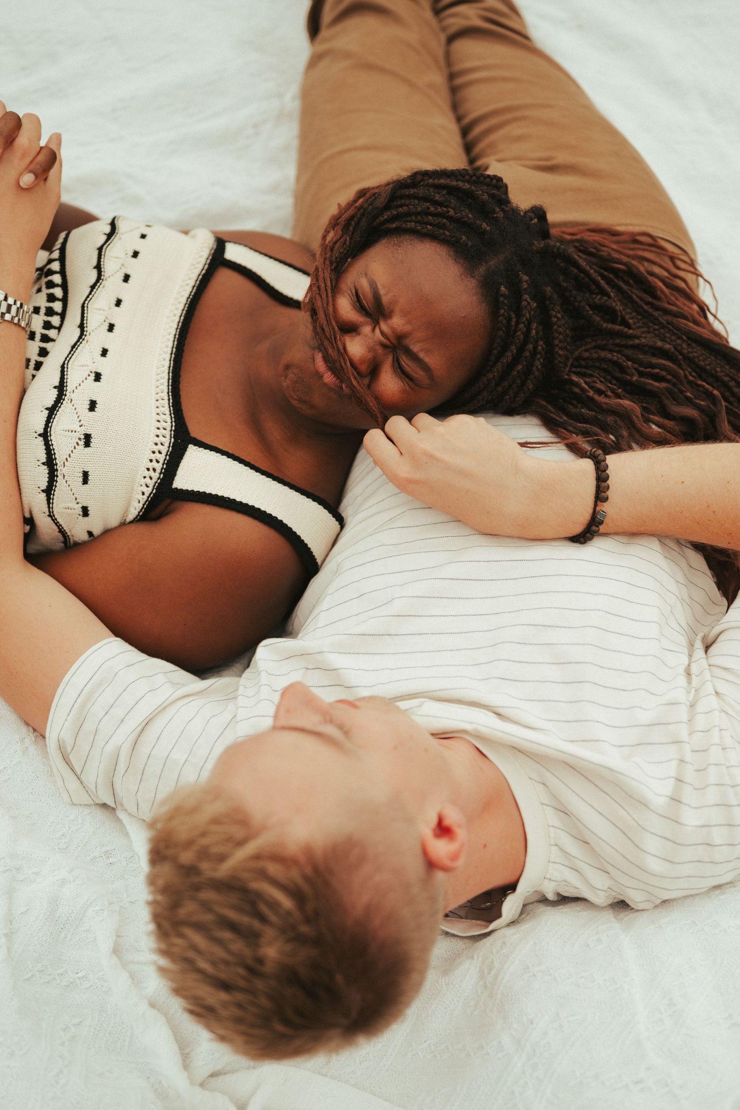 A couple lies together on white bedding sharing an intimate moment.
