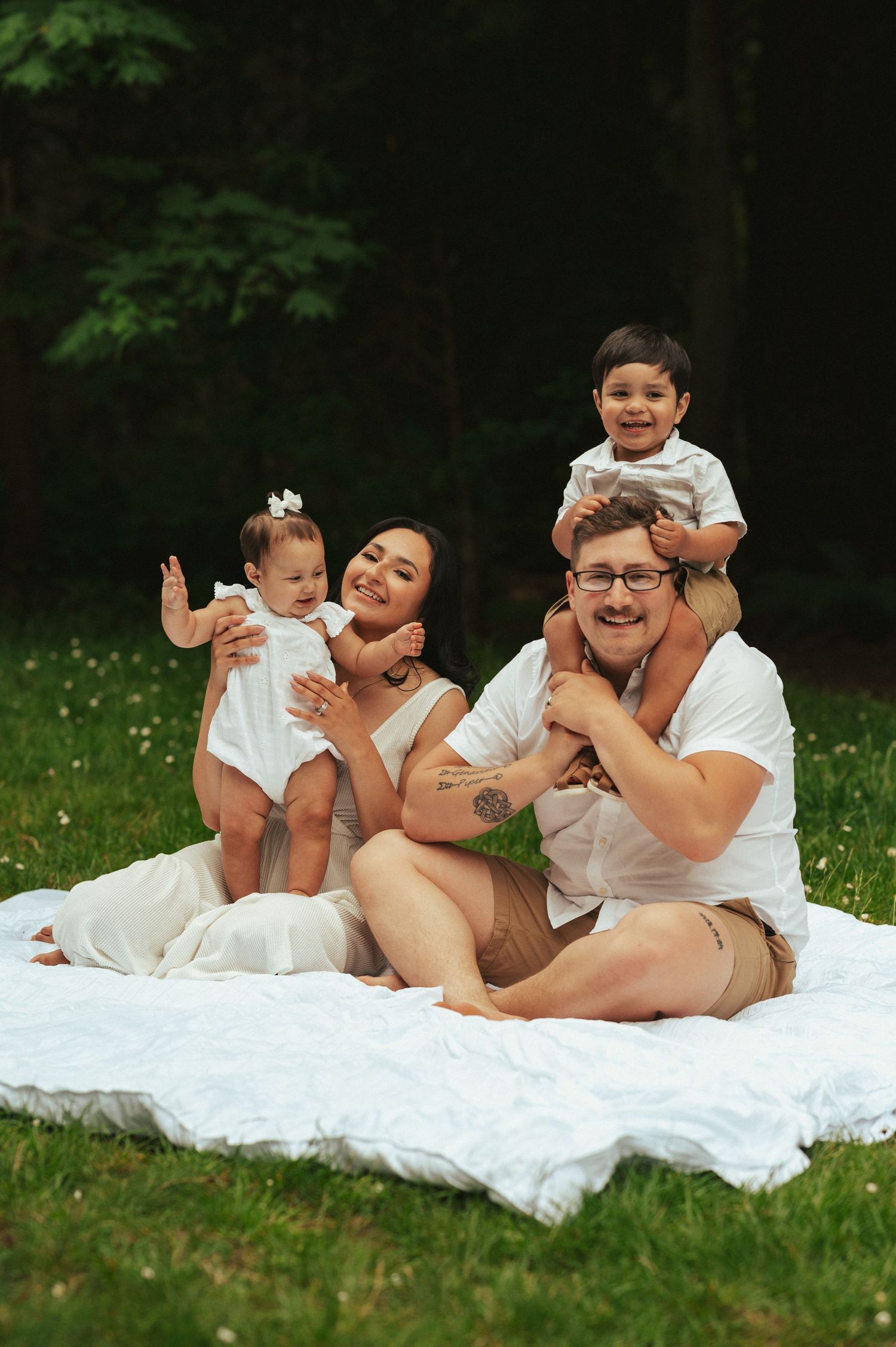 A joyful family moment captured on a white blanket in a grassy outdoor setting.
