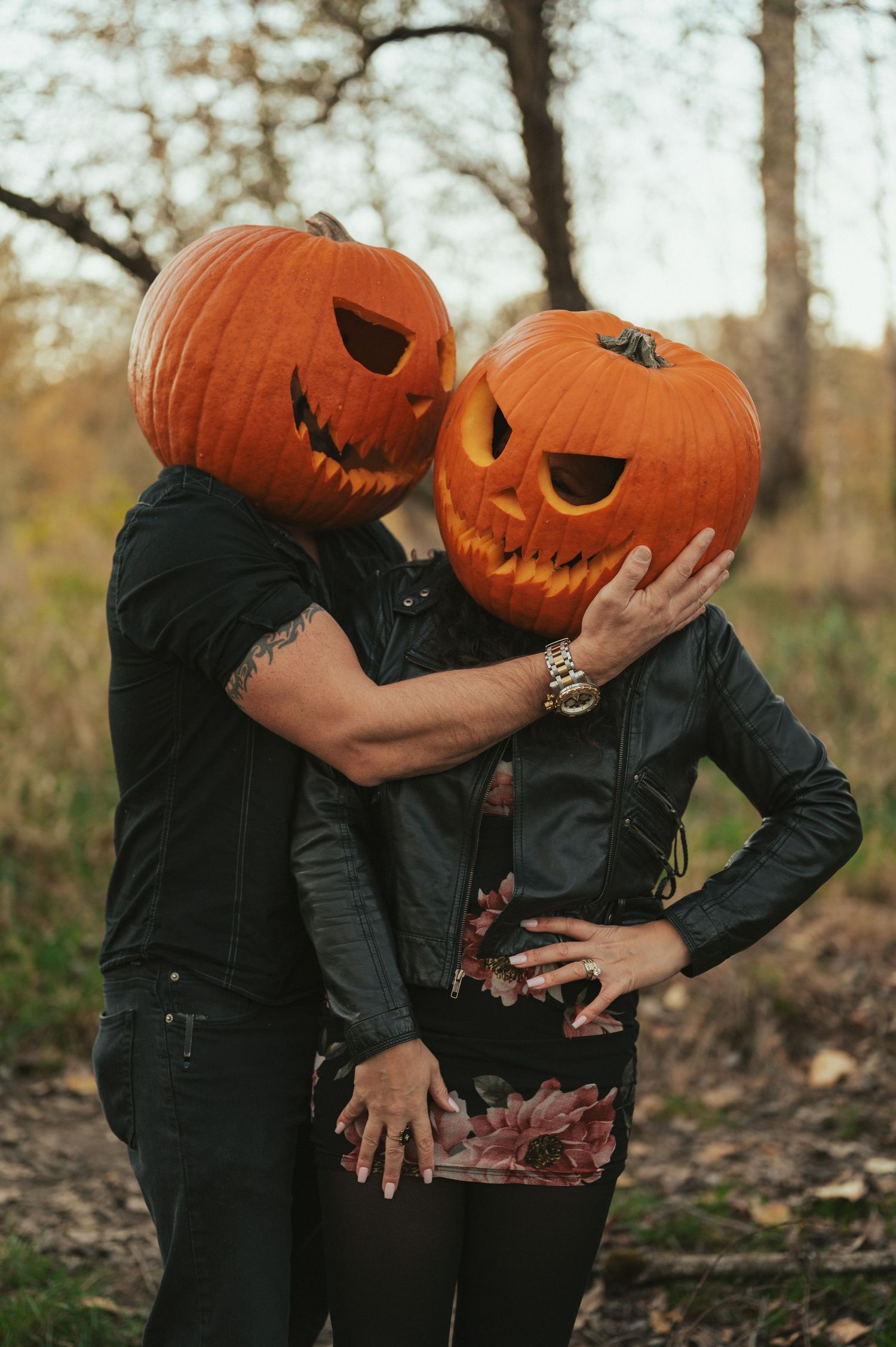 Two carved jack o'lantern pumpkins with mischievous expressions on people wearing black leather jackets in autumn setting.