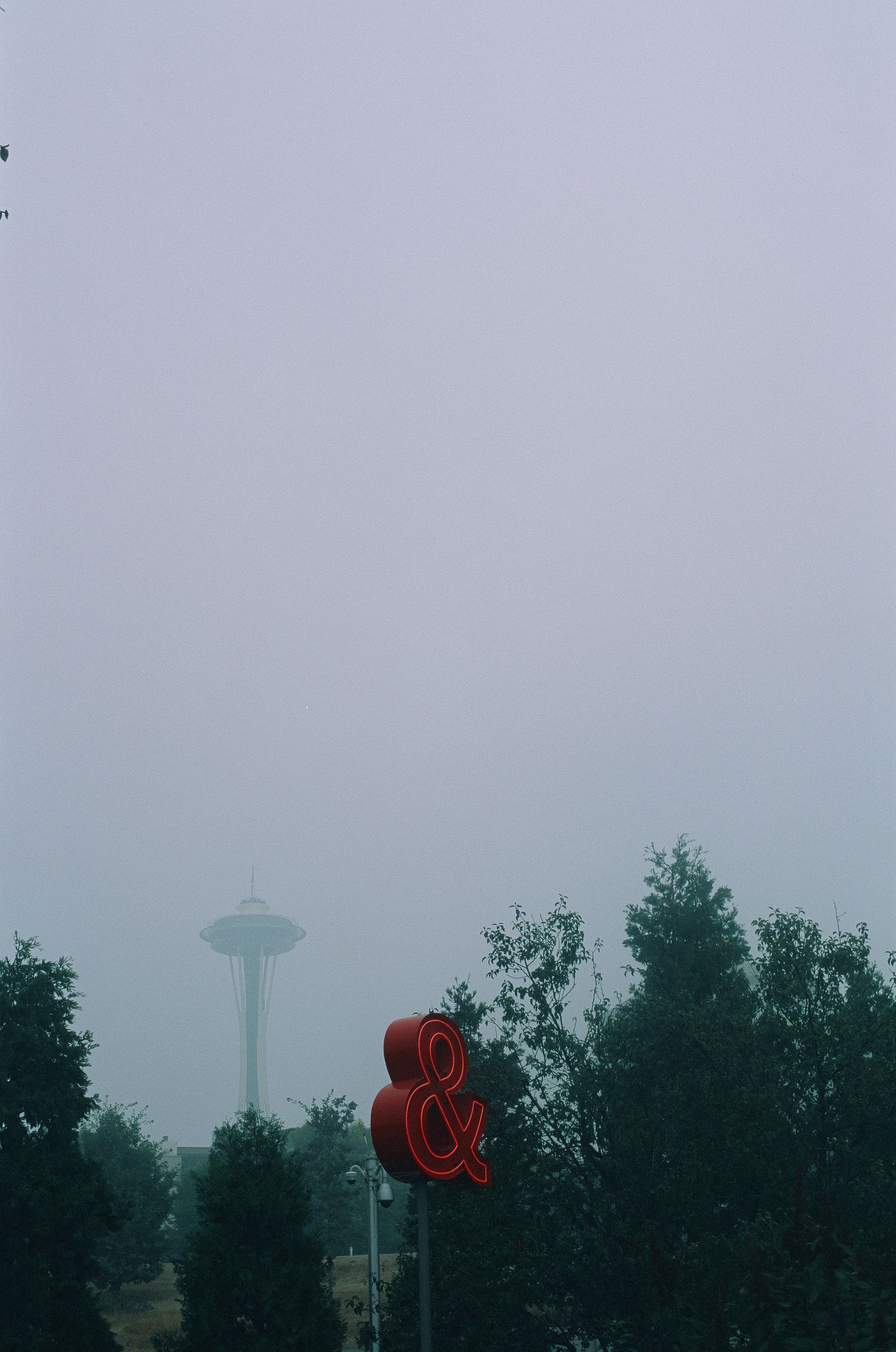 A red ampersand sign with Seattle's Space Needle visible in foggy background.