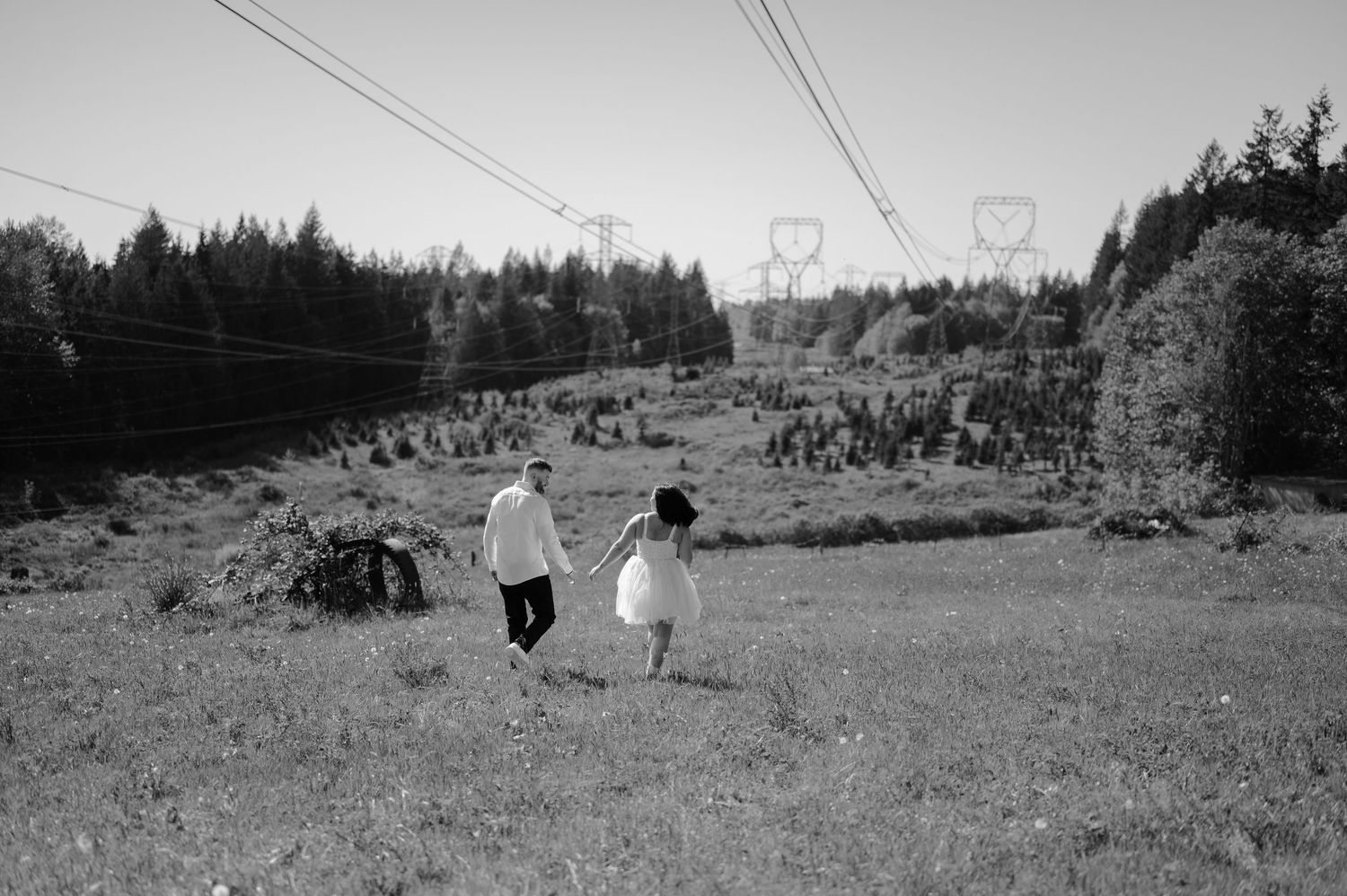 A couple runs through a grassy field with power lines overhead in black and white photography.