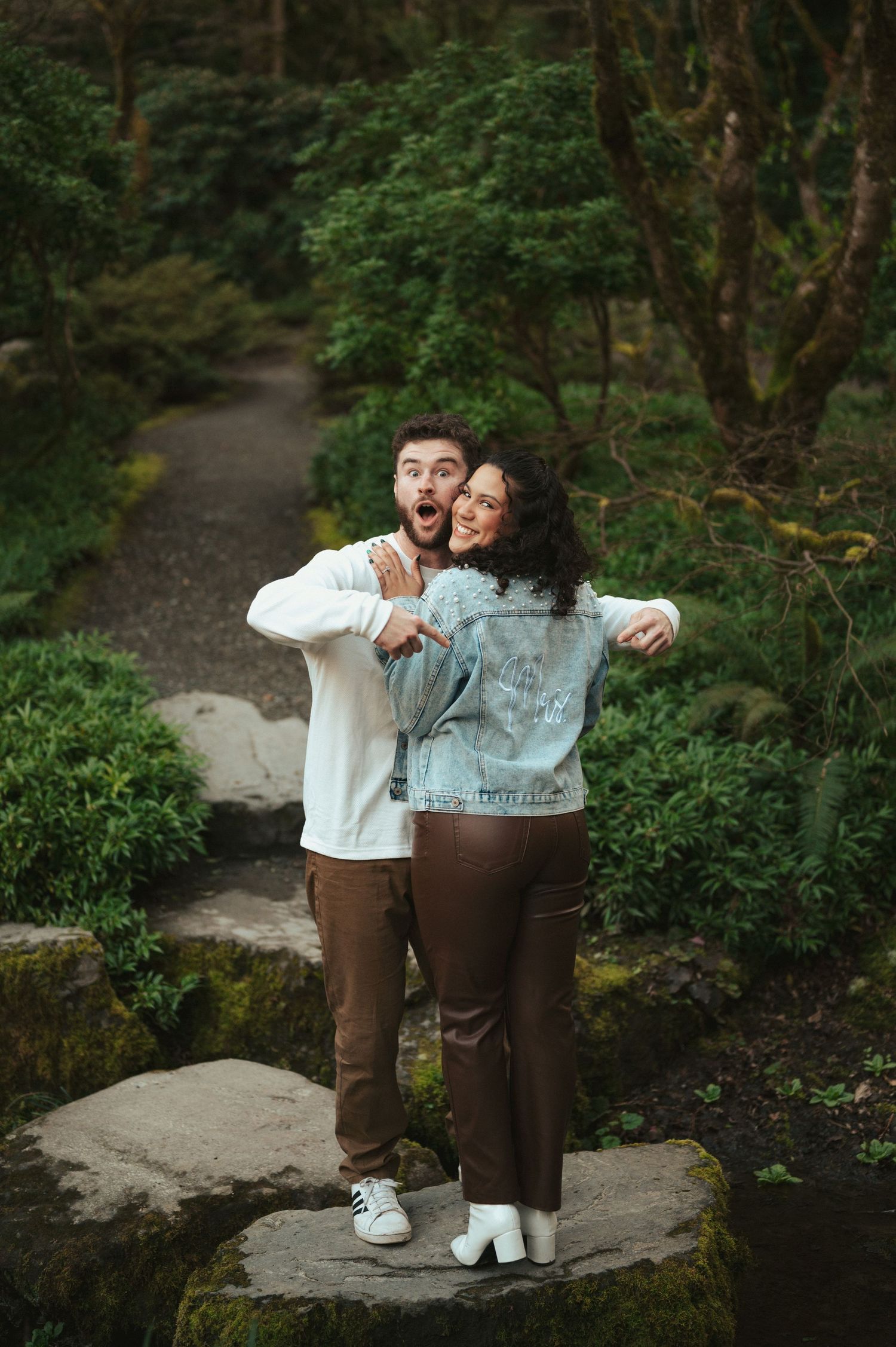 Happy couple sharing playful moments on stone path in lush garden setting.