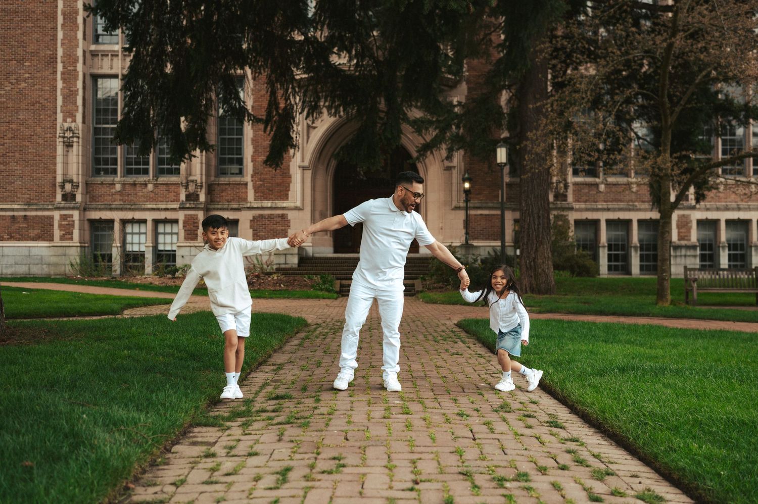 Three people in white outfits playing together on a brick path in front of a historic building.