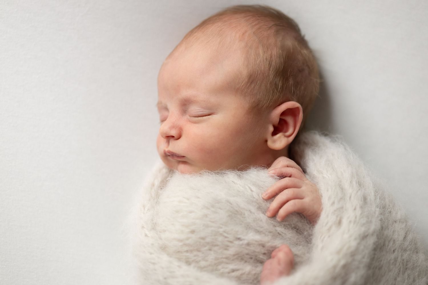 Peaceful newborn baby sleeping wrapped in white fluffy knit swaddle on white background.