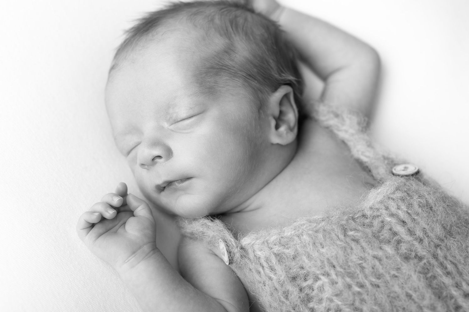 Peaceful sleeping newborn baby in a fuzzy knit romper, black and white portrait. photographe naissance chavanoz lyon