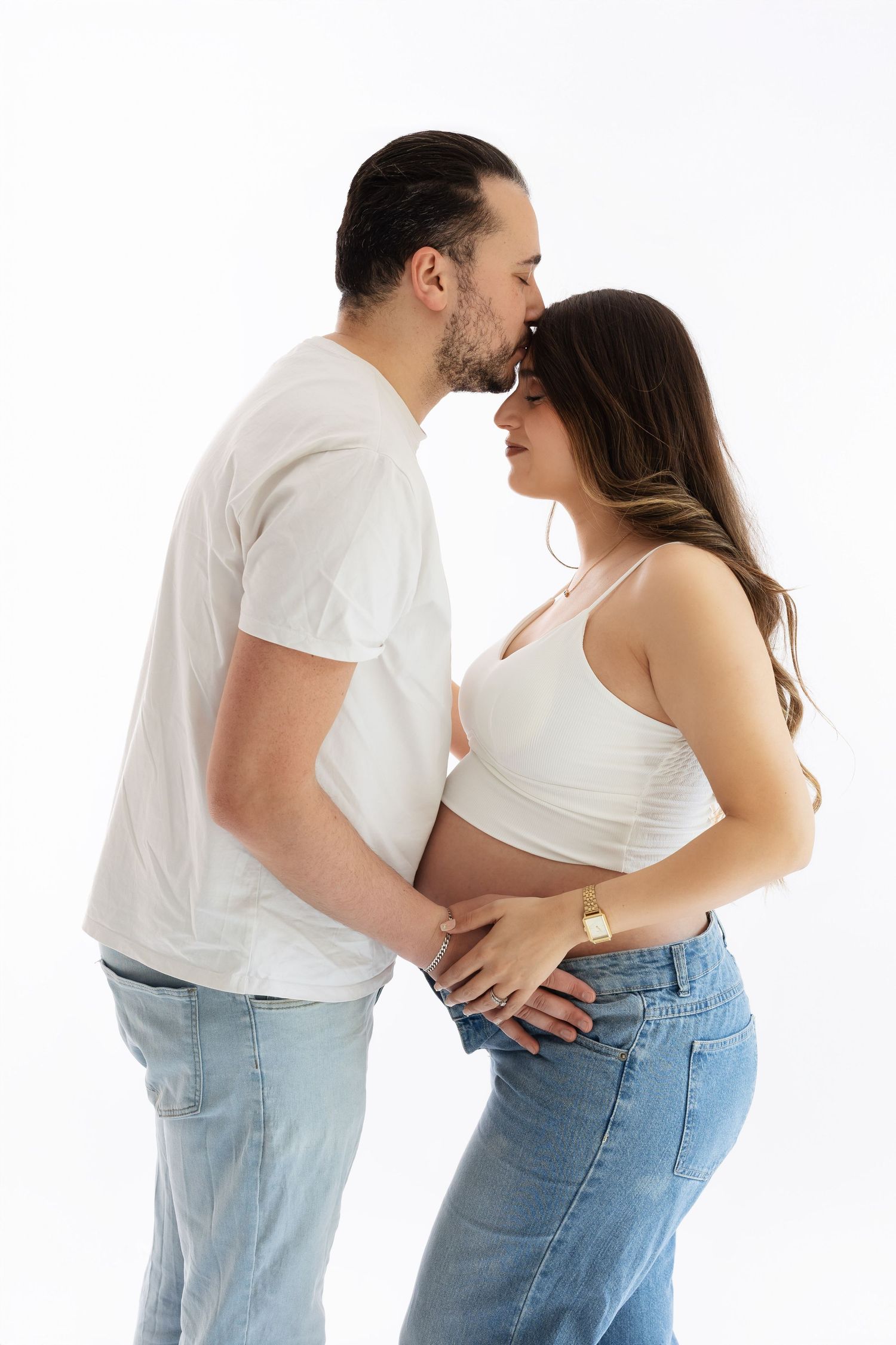 Couple sharing a tender kiss, man in white tee embracing pregnant woman in white crop top and jeans. photographe grossesse chavanoz lyon