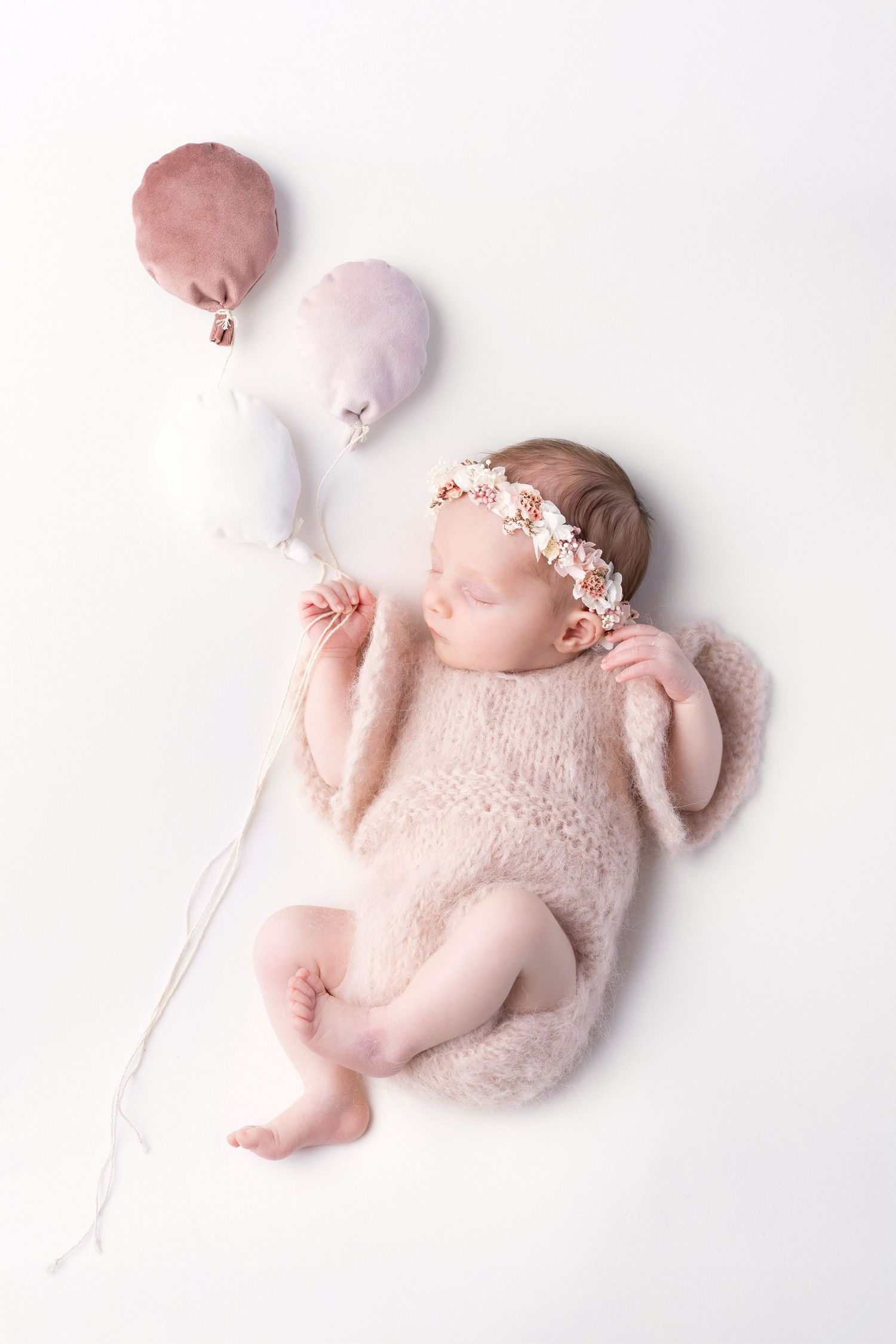Newborn baby girl in pink knit romper with floral crown holding decorative fabric balloons. photographe naissance chavanoz lyon