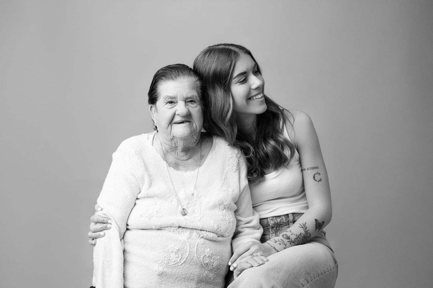Black and white portrait of elderly grandmother and young granddaughter smiling together in studio.