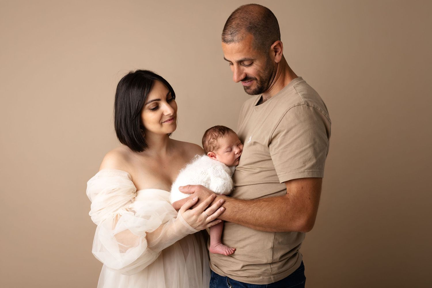 New parents tenderly hold their swaddled newborn baby during a professional studio portrait session.