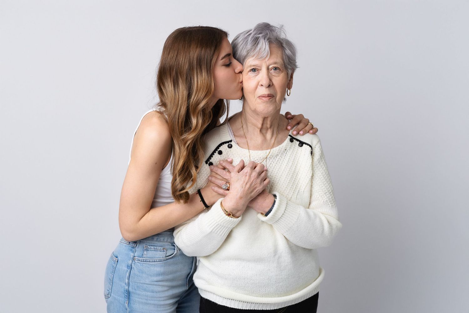 Young woman kissing elderly grandmother on cheek while embracing her in heartfelt studio portrait.