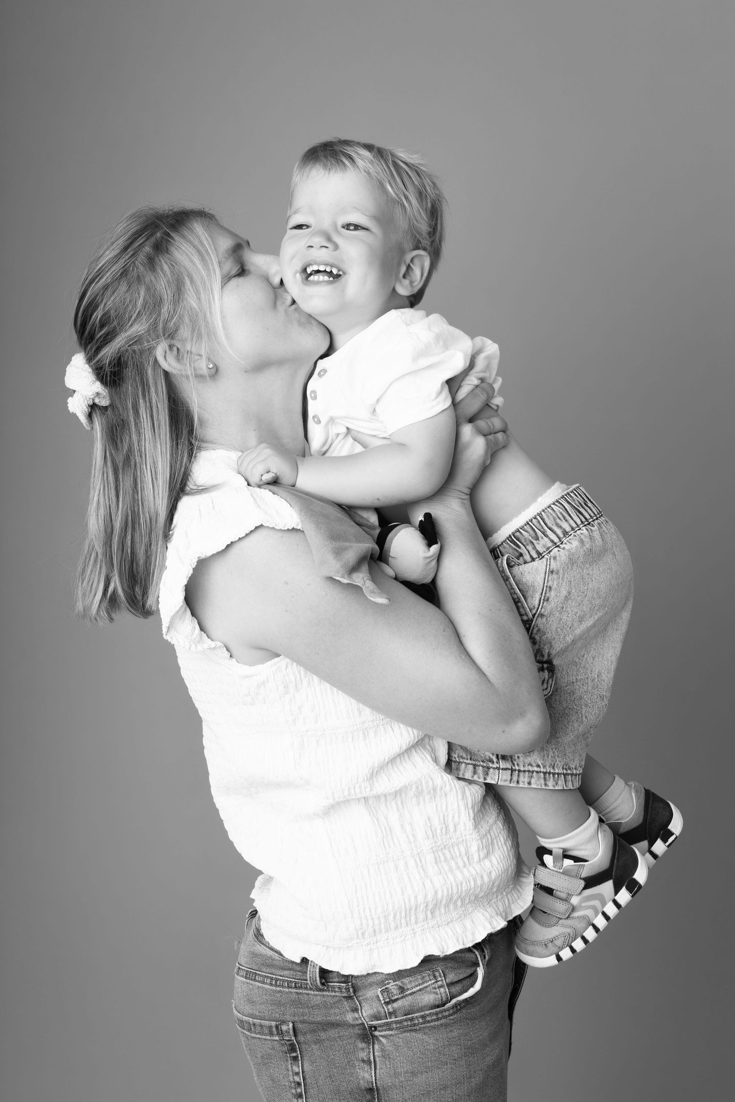 Black and white photo of a smiling mother kissing her laughing toddler child while lifting them up.