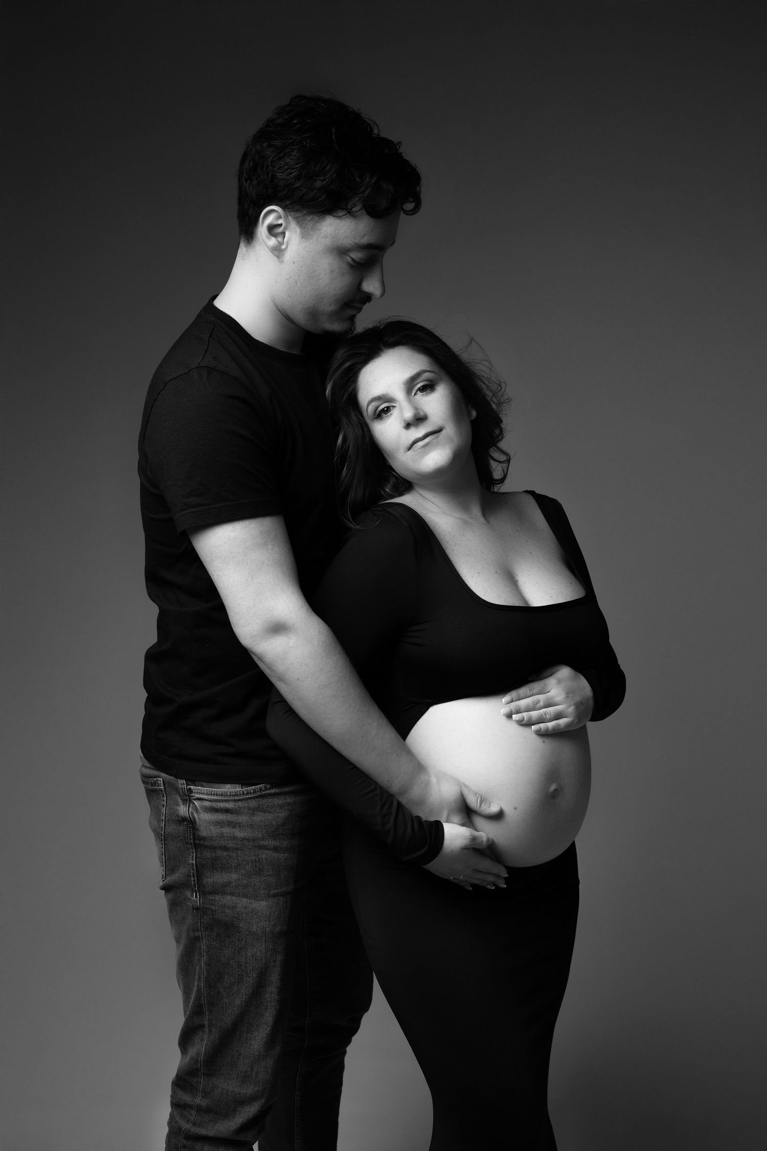 Black and white photo of couple embracing, man tenderly holding pregnant womans bare belly. photographe grossesse chavanoz lyon