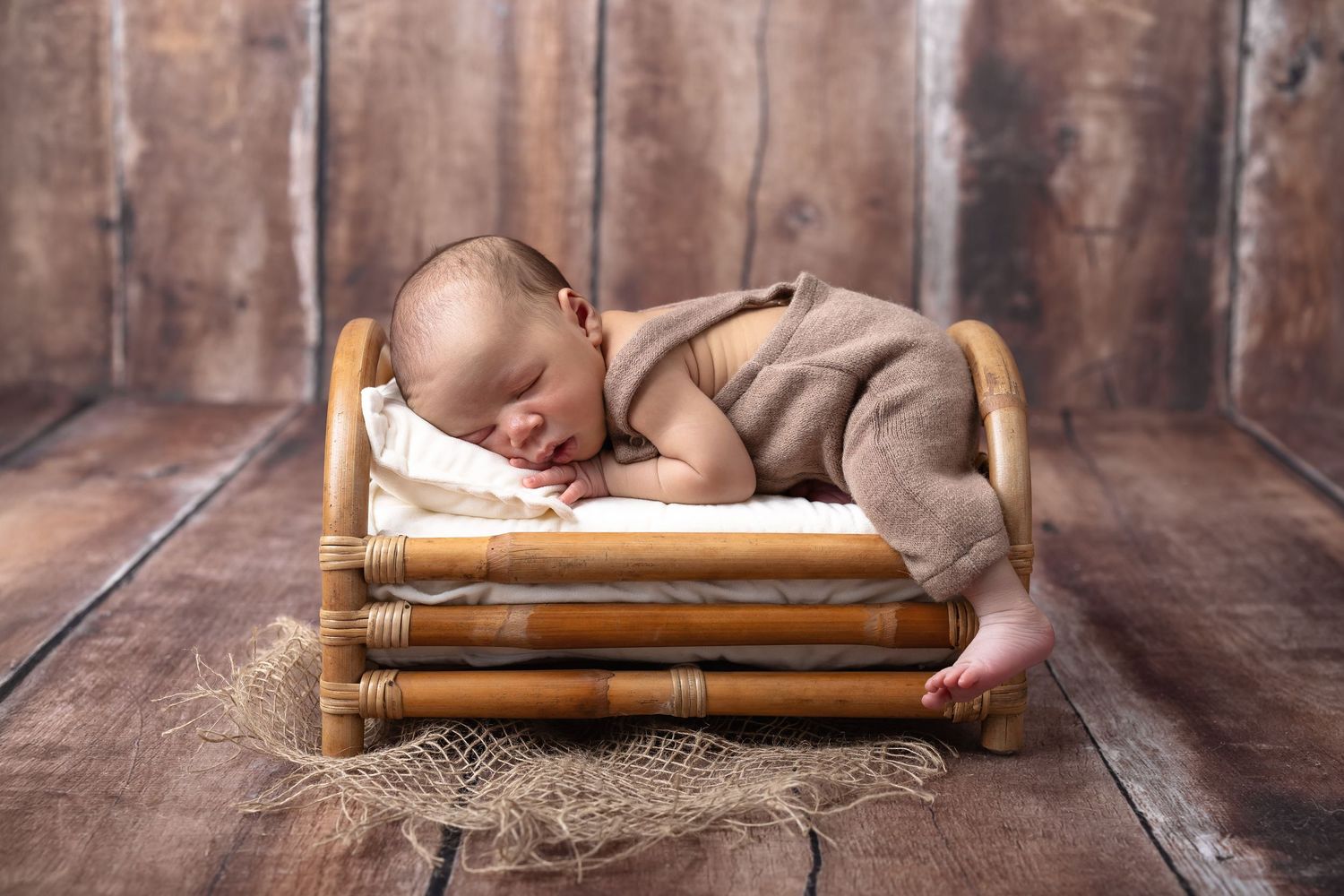 Newborn baby sleeping peacefully on a tiny wooden bed with brown wrap.