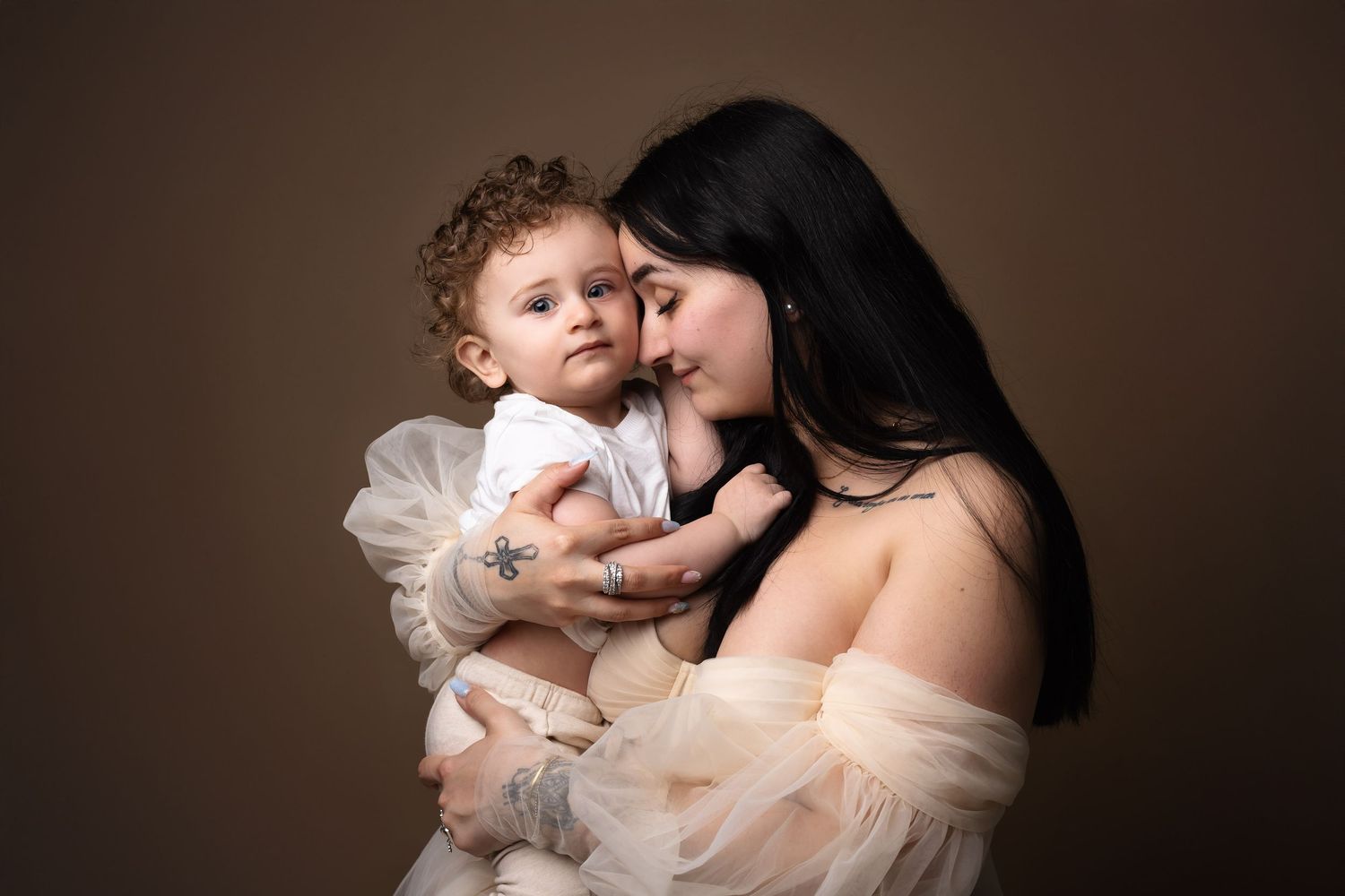 Loving mother in sheer blush gown tenderly holding and nuzzling her curly-haired baby. photographe grossesse chavanoz lyon