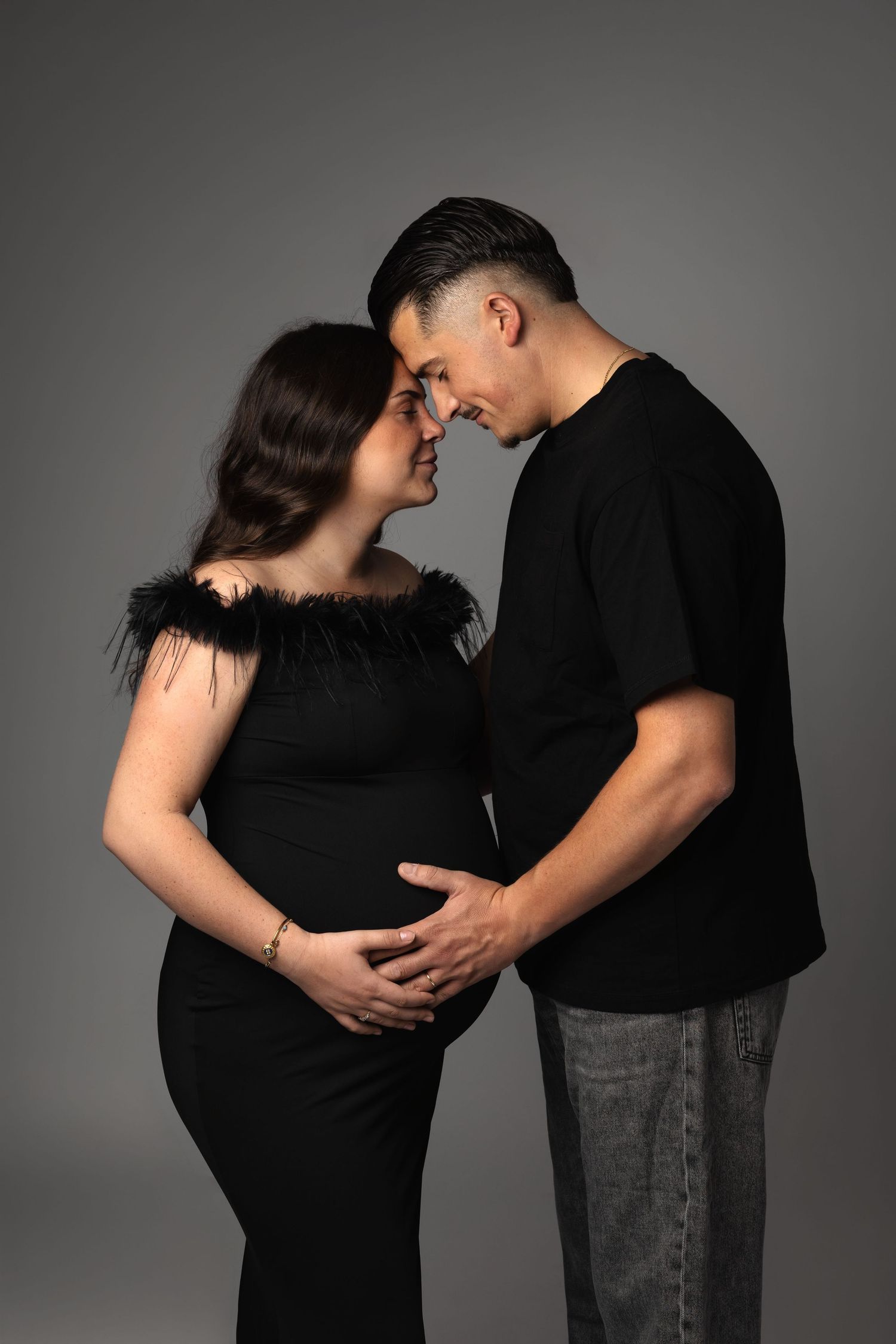 A couple in matching black outfits sharing a tender moment, with the pregnant woman's baby bump cradled by both partners.