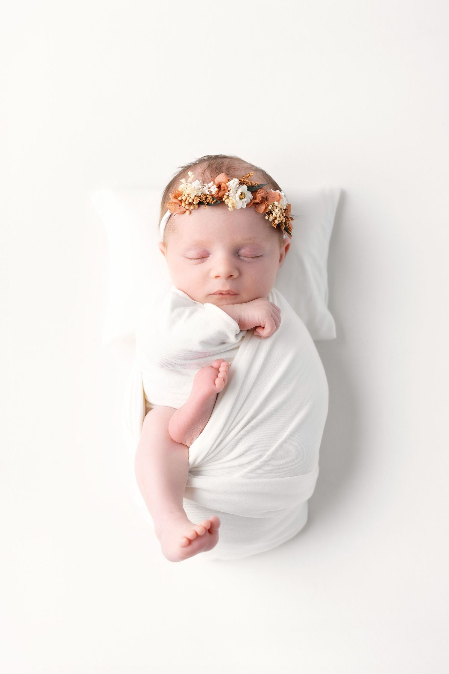 Sleeping newborn baby girl swaddled in white wrap with floral crown on white background. photographe naissance chavanoz lyon