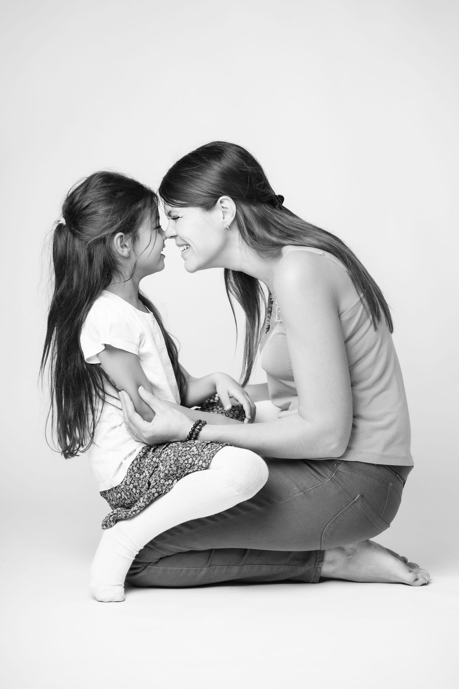 Black and white portrait of a smiling mother and young daughter sharing a tender nose-to-nose moment.
