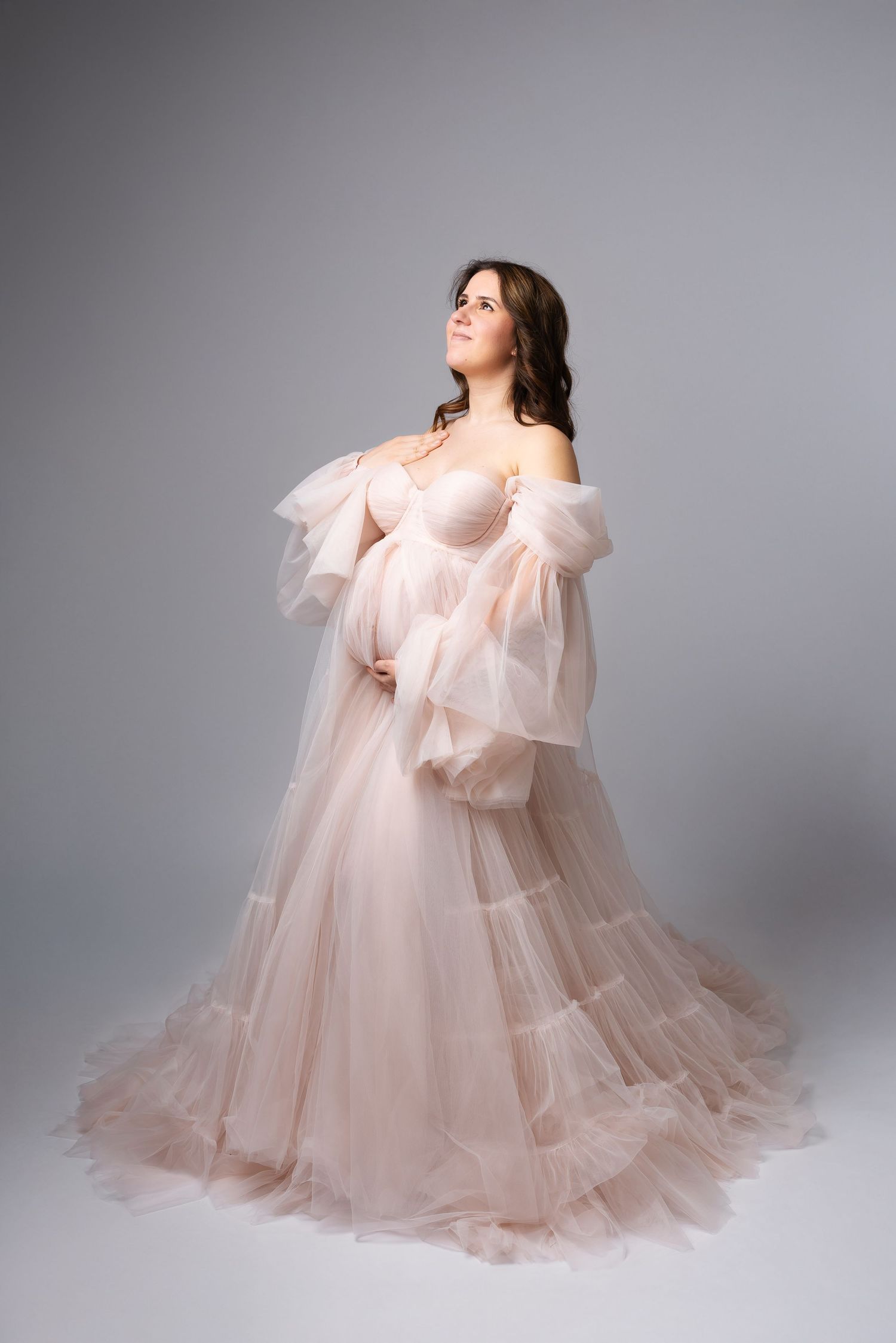Elegant pregnant woman in flowing blush pink tulle maternity gown on grey background. photographe grossesse chavanoz lyon