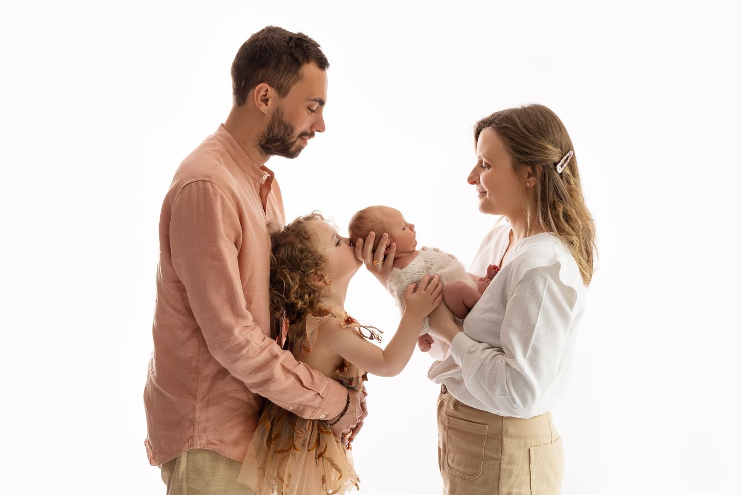 Happy family with father, mother, curly-haired toddler, and newborn baby posing on white background. photographe naissance chavanoz lyon