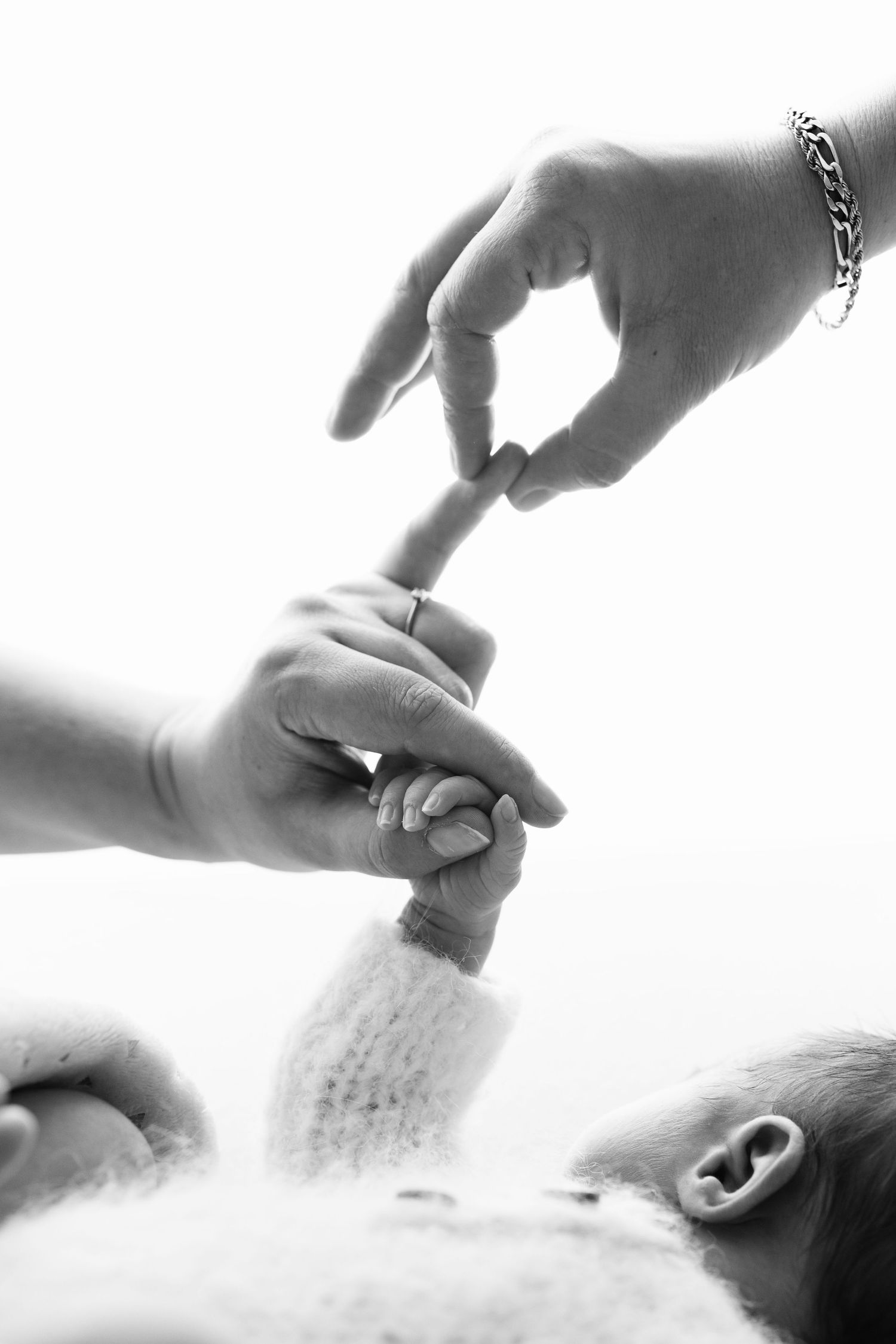 Black and white photo of a newborn baby grasping an adult finger, symbolizing new life and parental bond.