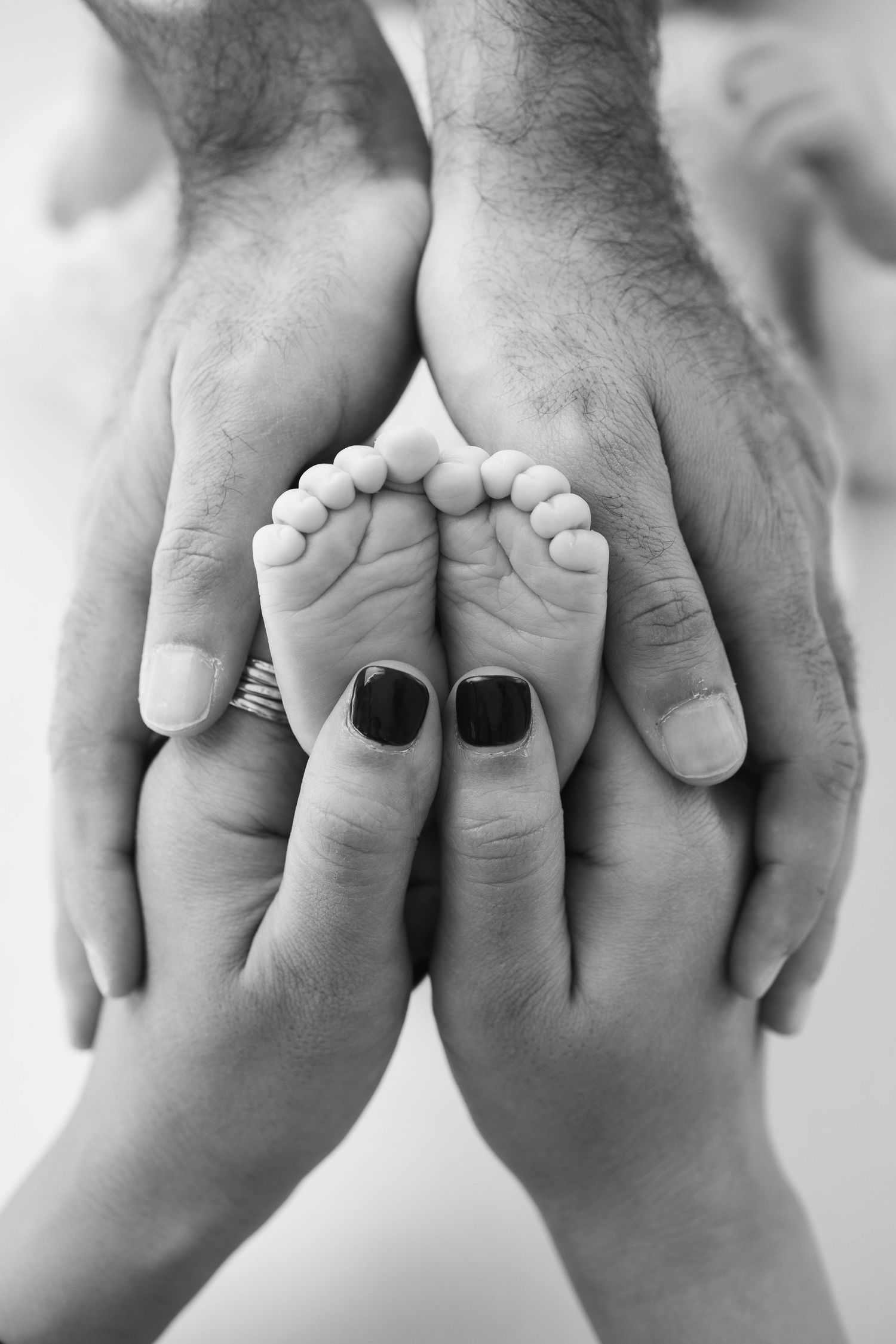 Black and white photo of tiny newborn baby feet cradled gently in parents hands. séance naissance chavanoz lyon
