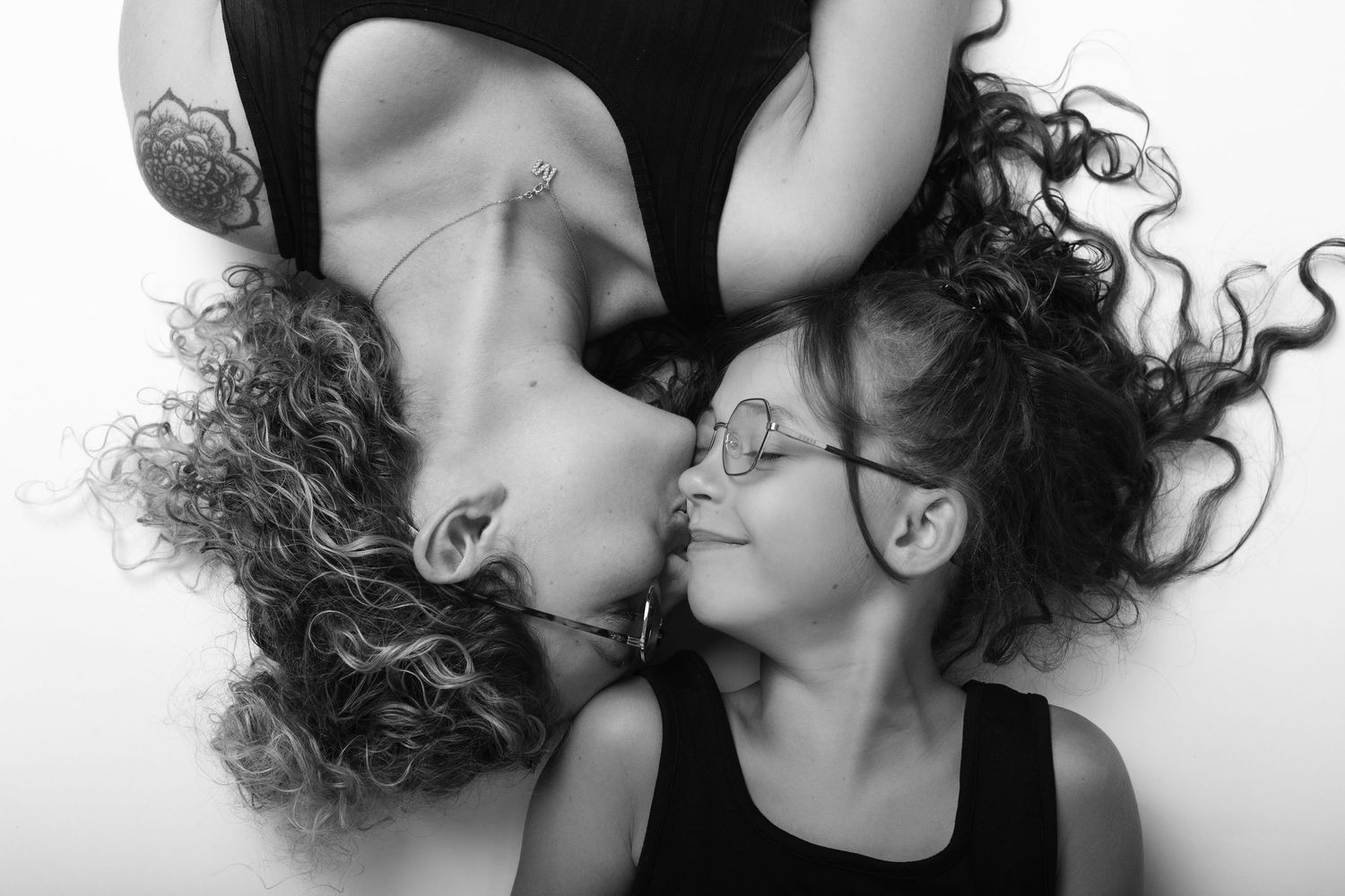 Black and white overhead portrait of a curly-haired mother and her daughter lying head to head.