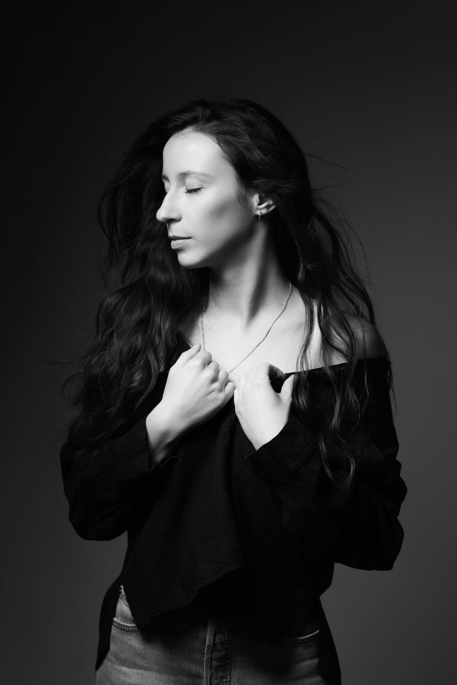 Black and white portrait of woman with long dark hair in black blouse, eyes closed.