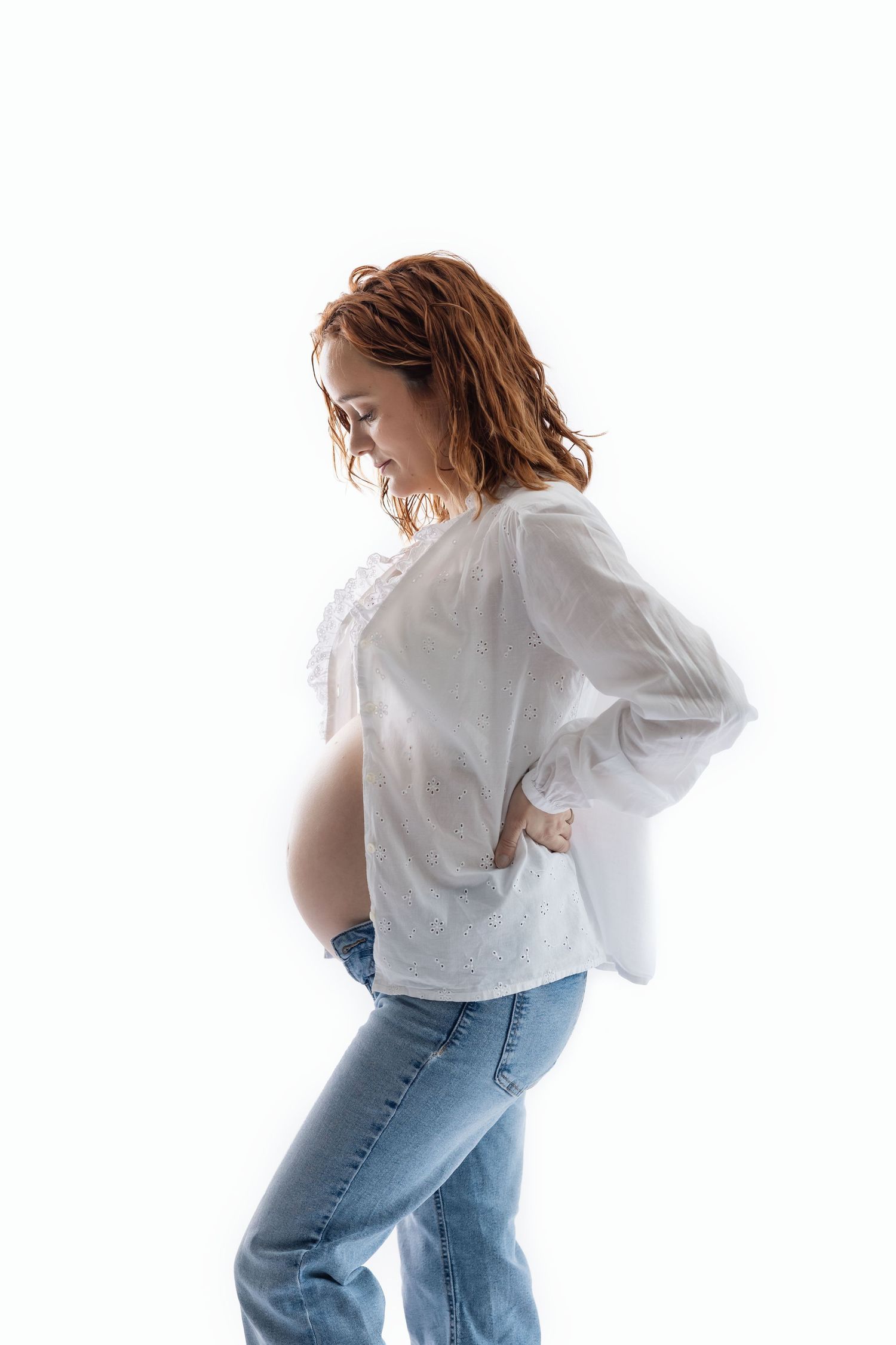 Pregnant woman in white blouse and jeans showing baby bump against white background.