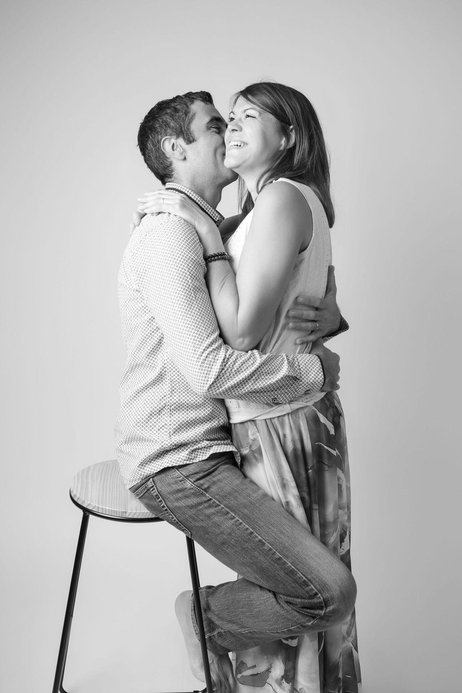 Black and white studio portrait of a couple sharing a romantic embrace, woman standing beside seated man.