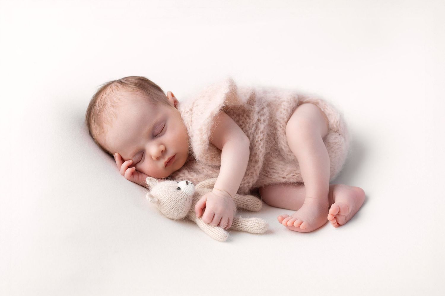 Sleeping newborn baby in cream knit romper cuddling a small stuffed bunny toy. photographe naissance chavanoz lyon
