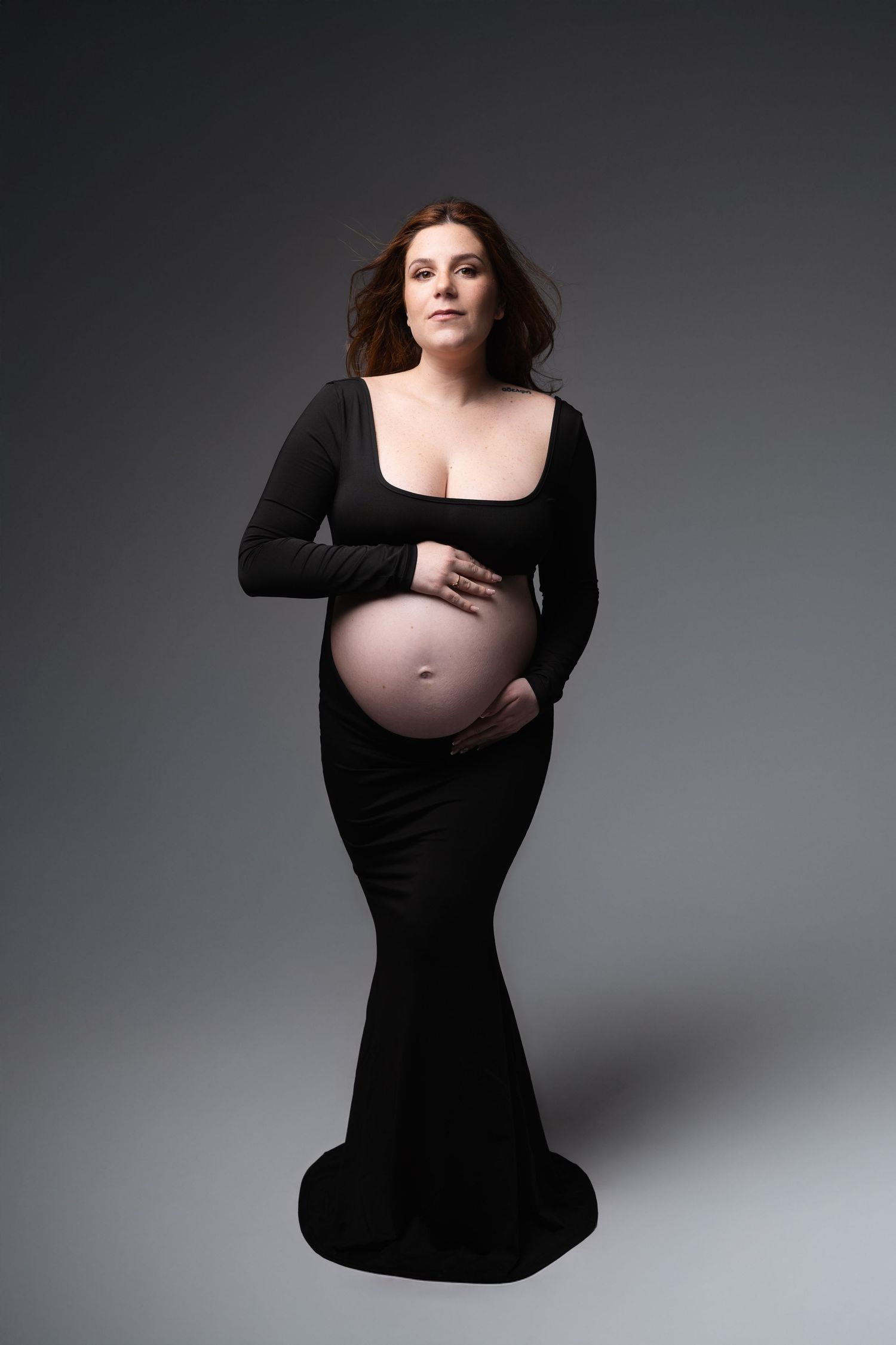 Pregnant woman in black open-front gown showcasing her bare baby bump in a studio setting. photographe grossesse chavanoz lyon