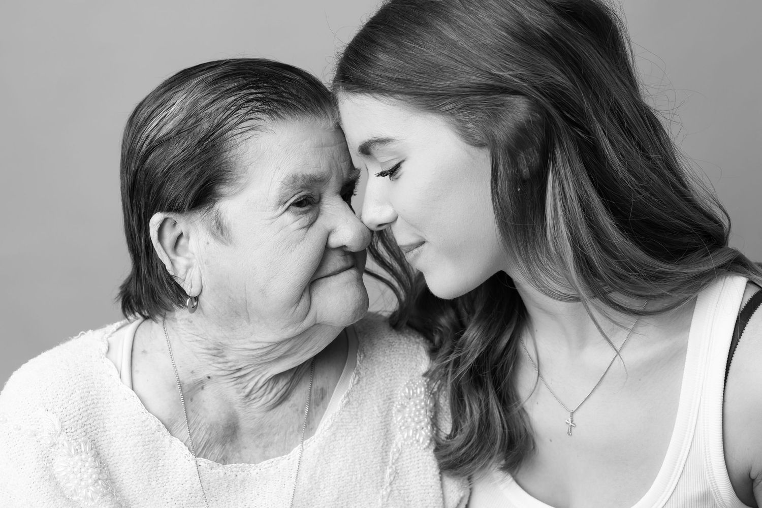 Tender black and white close-up portrait of elderly grandmother and young granddaughter touching foreheads.