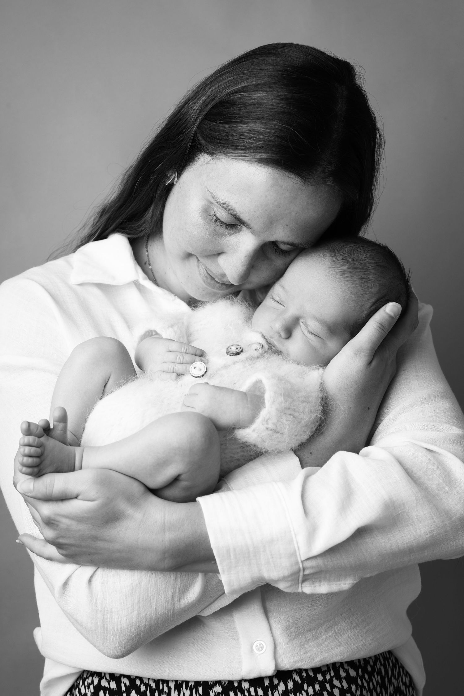 Black and white photo of a smiling mother tenderly cradling her sleeping newborn baby close to her chest.