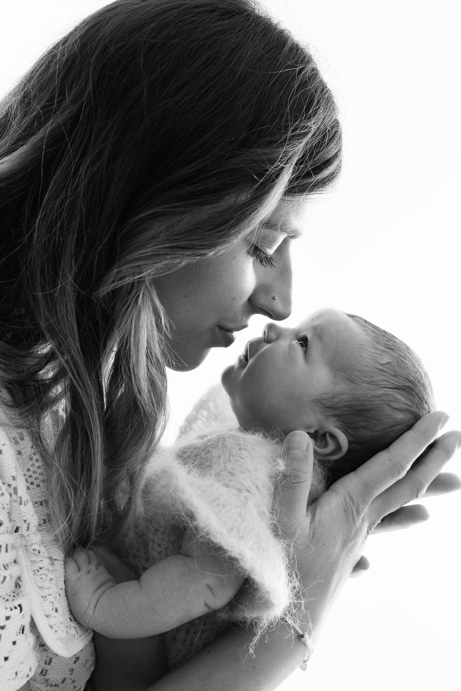 Black and white photo of a mother tenderly holding her newborn baby face to face in an intimate bonding moment.