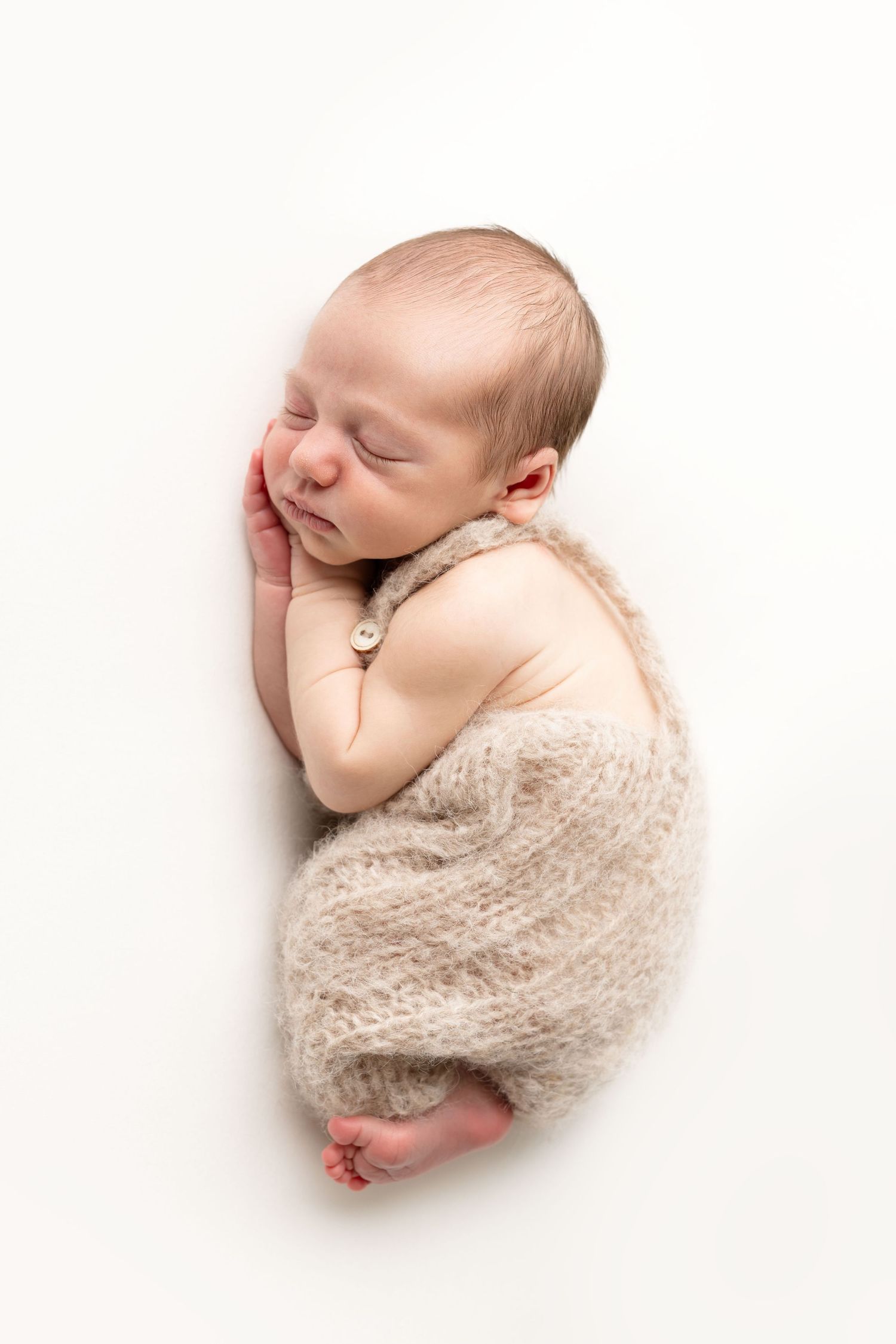 Sleeping newborn baby wrapped in a soft beige knit blanket on a white background.
