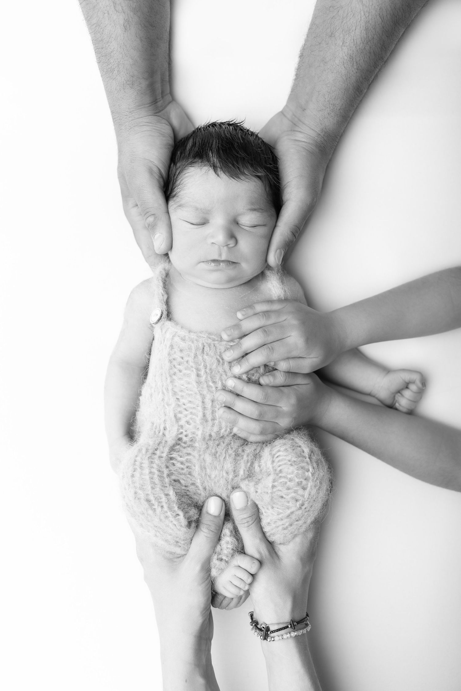 Black and white photo of sleeping newborn baby surrounded by loving family hands gently cradling them. photographe naissance chavanoz lyon
