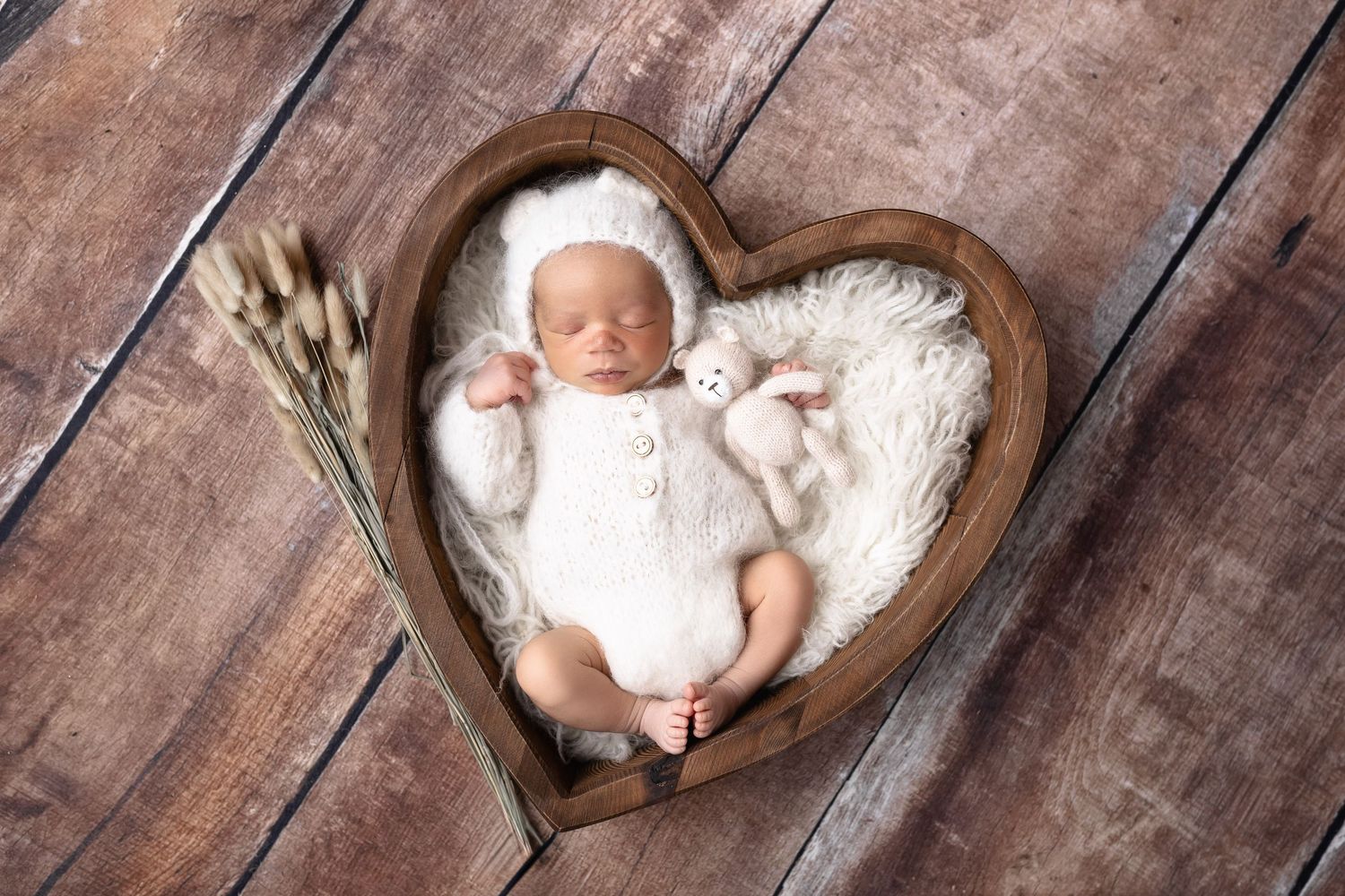 Newborn baby sleeping in a heart-shaped wooden bowl with white fur lining.