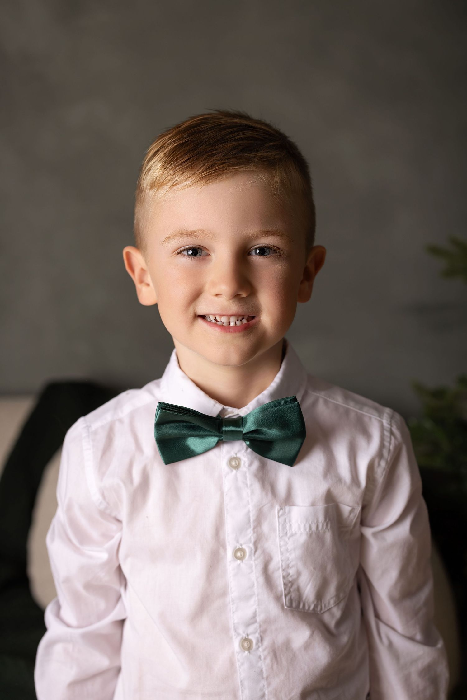 Smiling young boy in white dress shirt and green bow tie posing for a portrait photo.