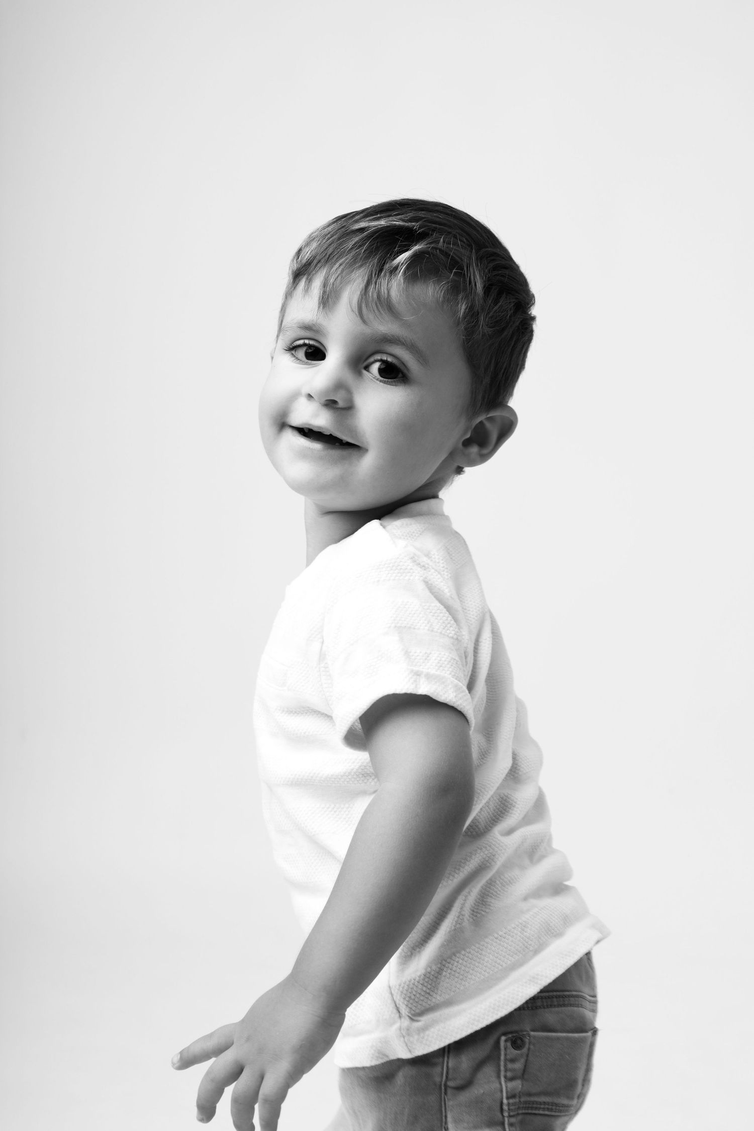 Black and white portrait of a happy toddler boy in a white t-shirt and jeans smiling over his shoulder.
