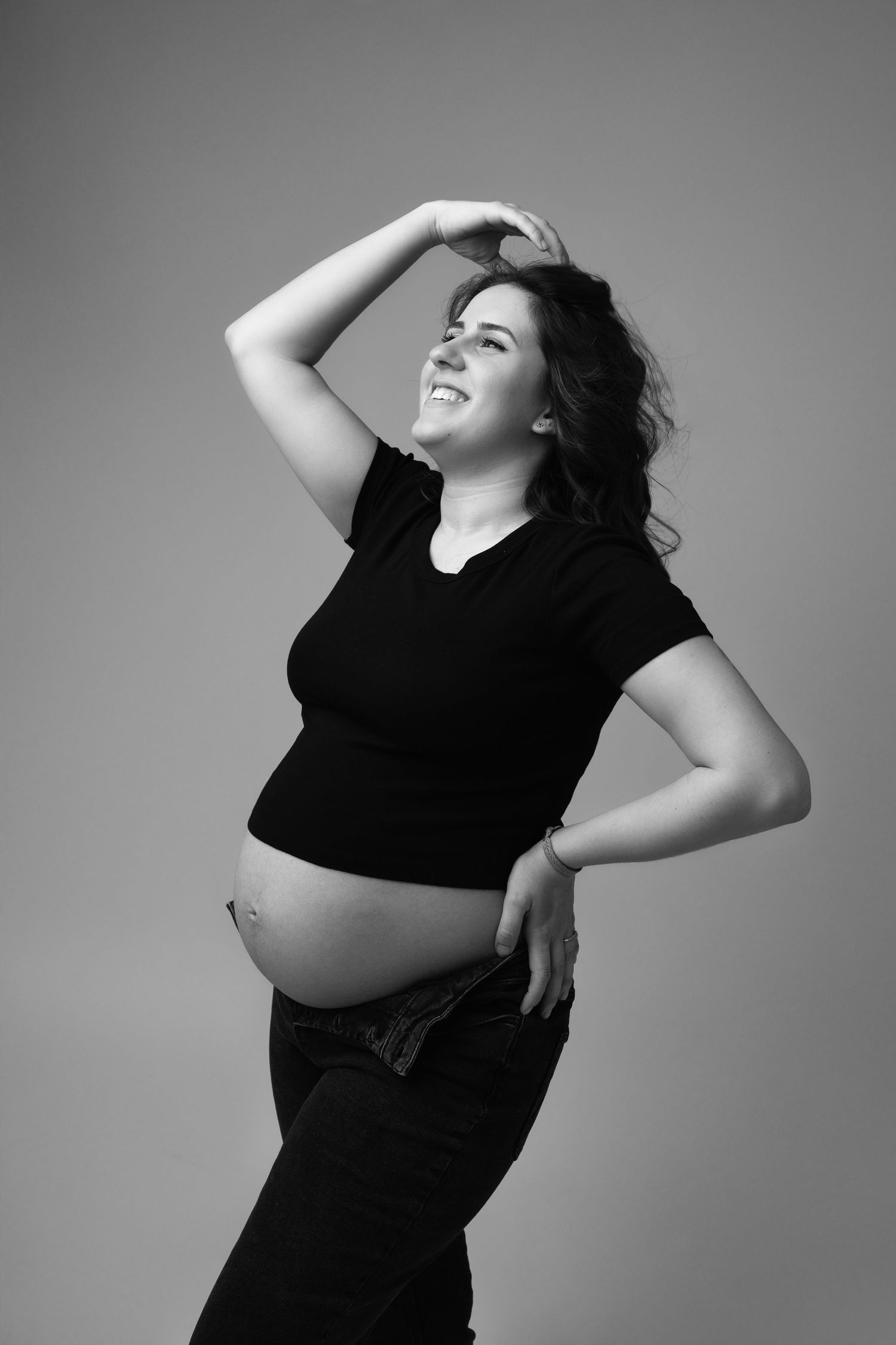Black and white portrait of smiling pregnant woman in black outfit showing baby bump. photographe grossesse chavanoz lyon