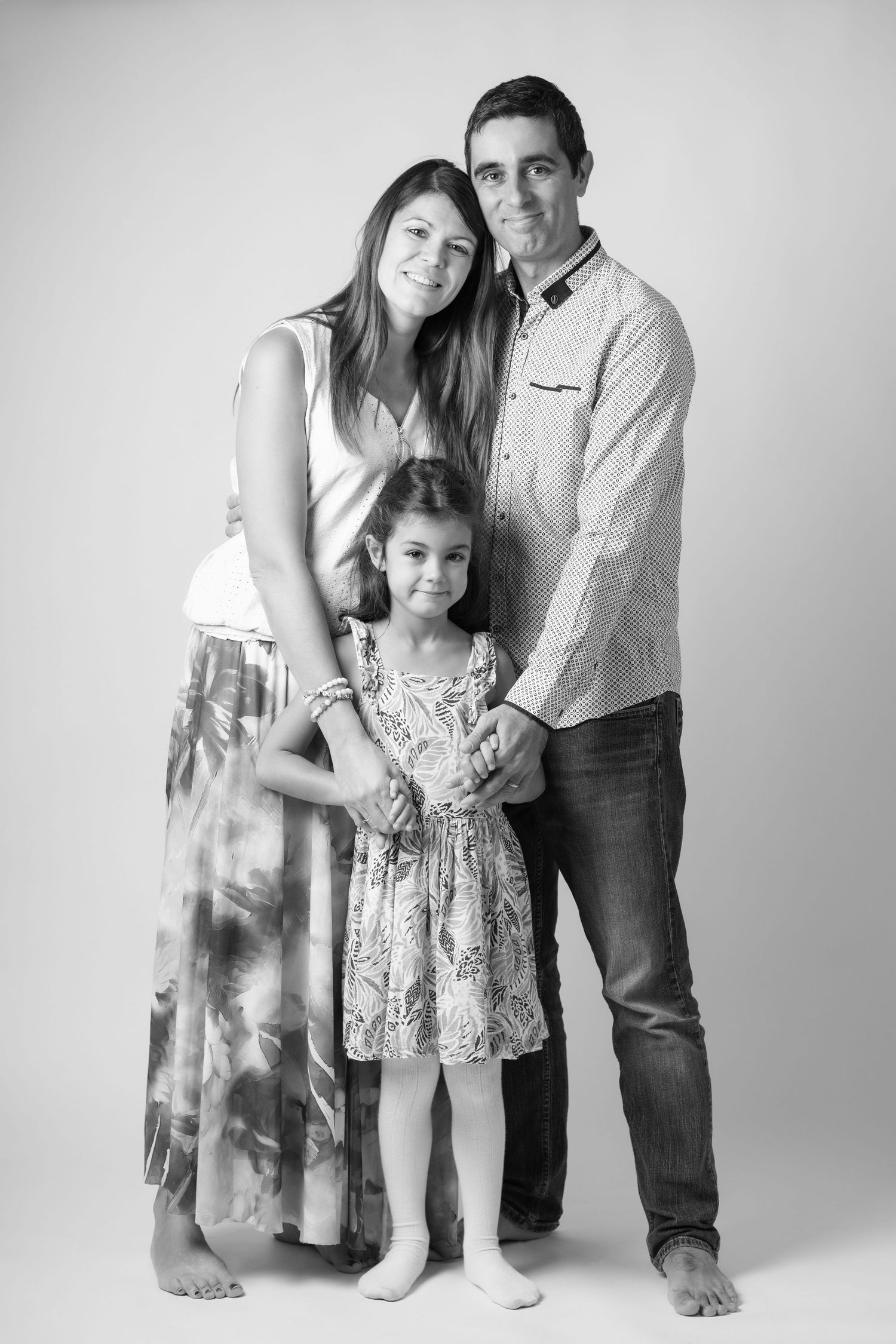 Black and white studio portrait of a family of three, parents standing with young daughter between them.