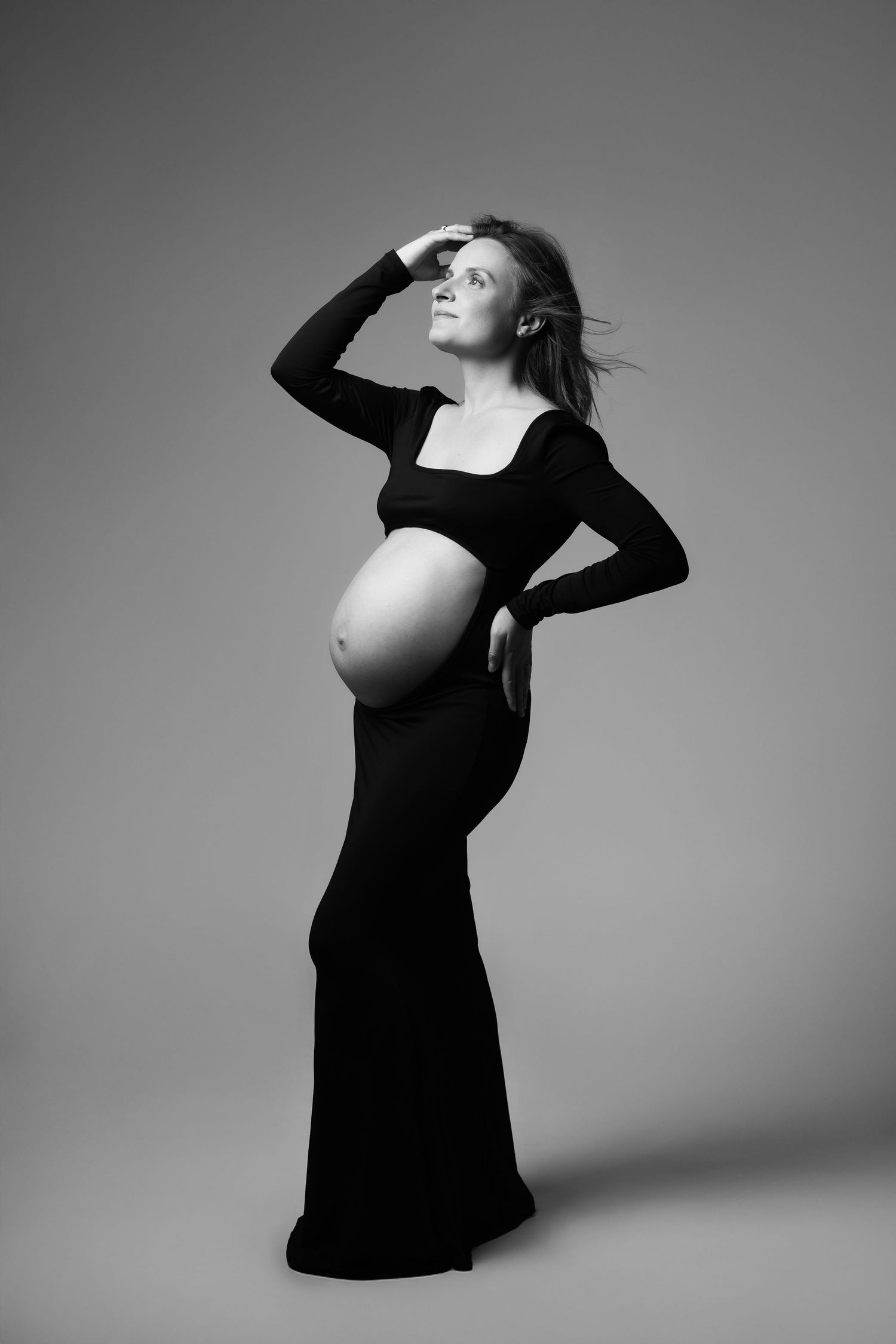 Black and white photo of a pregnant woman in a black gown posing elegantly in a studio setting.
