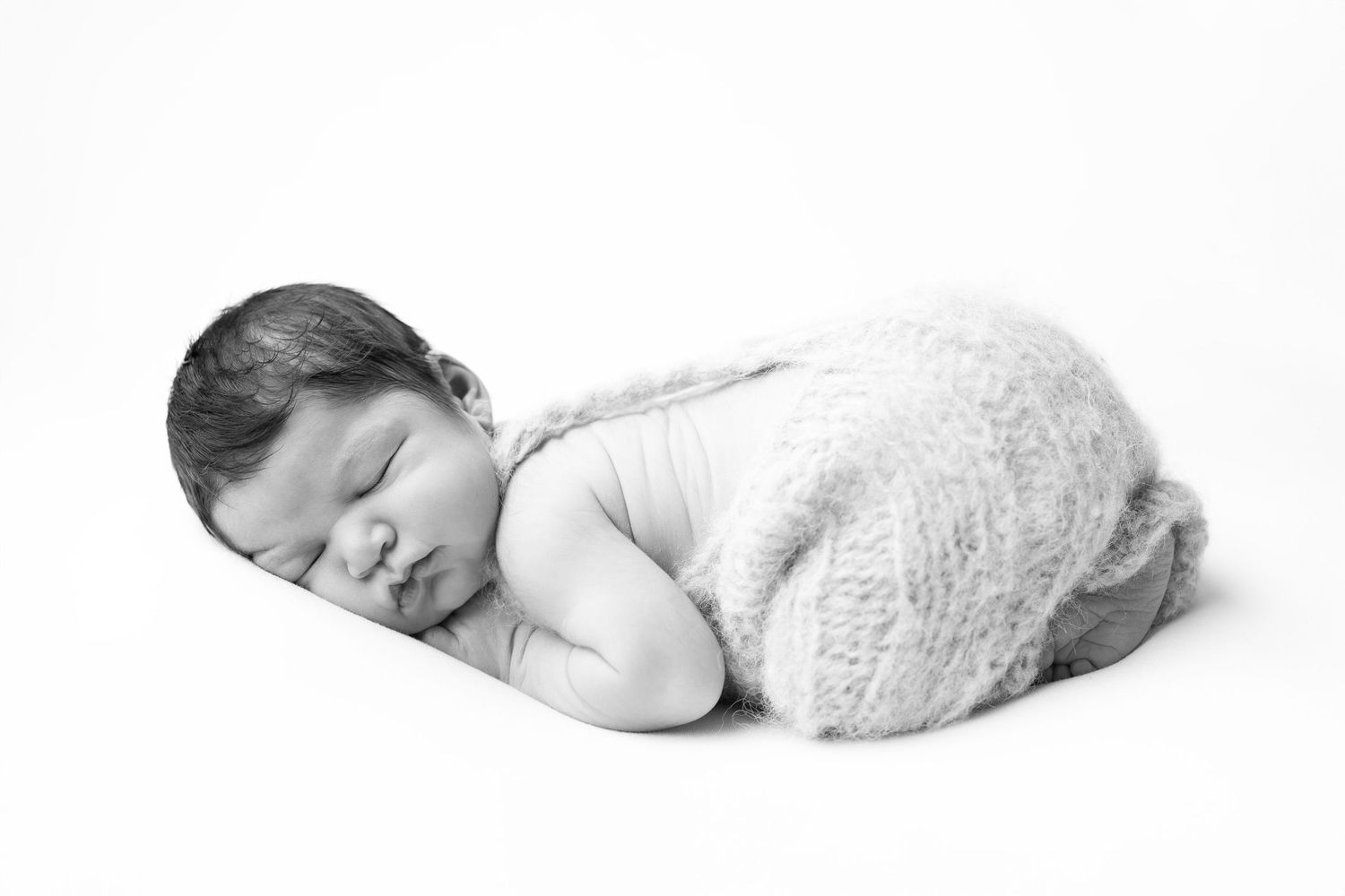 Sleeping newborn baby lying on stomach wrapped in soft fluffy knit blanket, black and white photography. photographe naissance chavanoz lyon