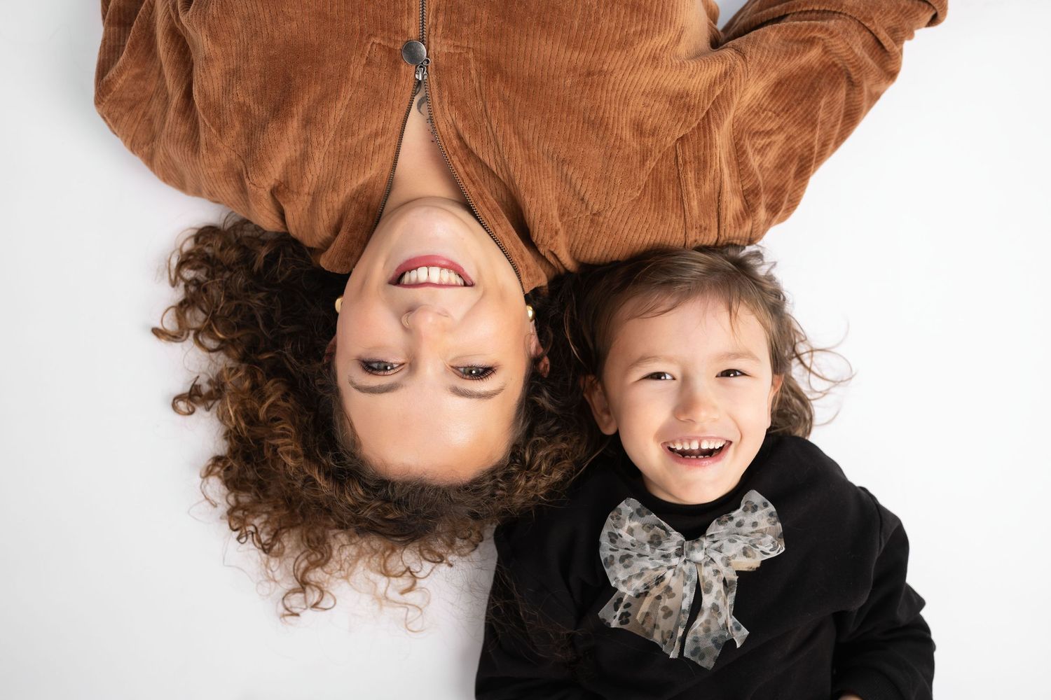 Overhead view of laughing mother and daughter lying on white floor smiling at camera.