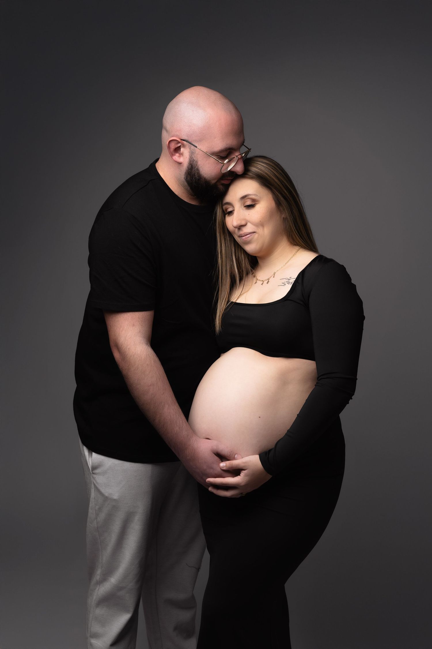 Expecting couple in black outfits tenderly cradling pregnant belly in studio. photographe grossesse chavanoz lyon
