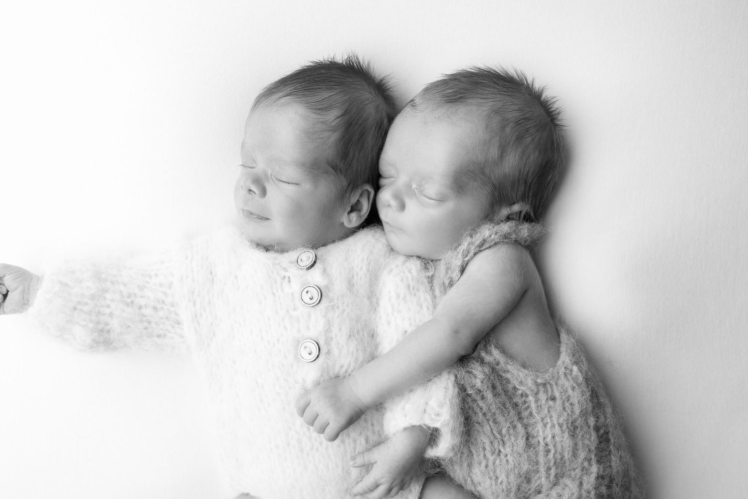 Black and white photo of sleeping newborn twins cuddled together in soft knit outfits. photographe naissance chavanoz lyon