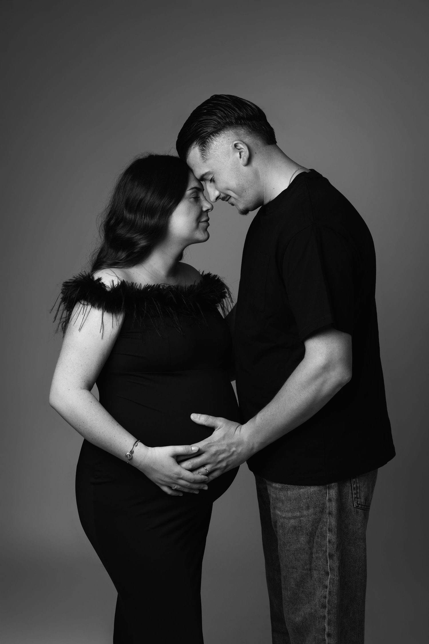 Black and white maternity photo of a couple tenderly touching foreheads while man cradles pregnant woman's belly.