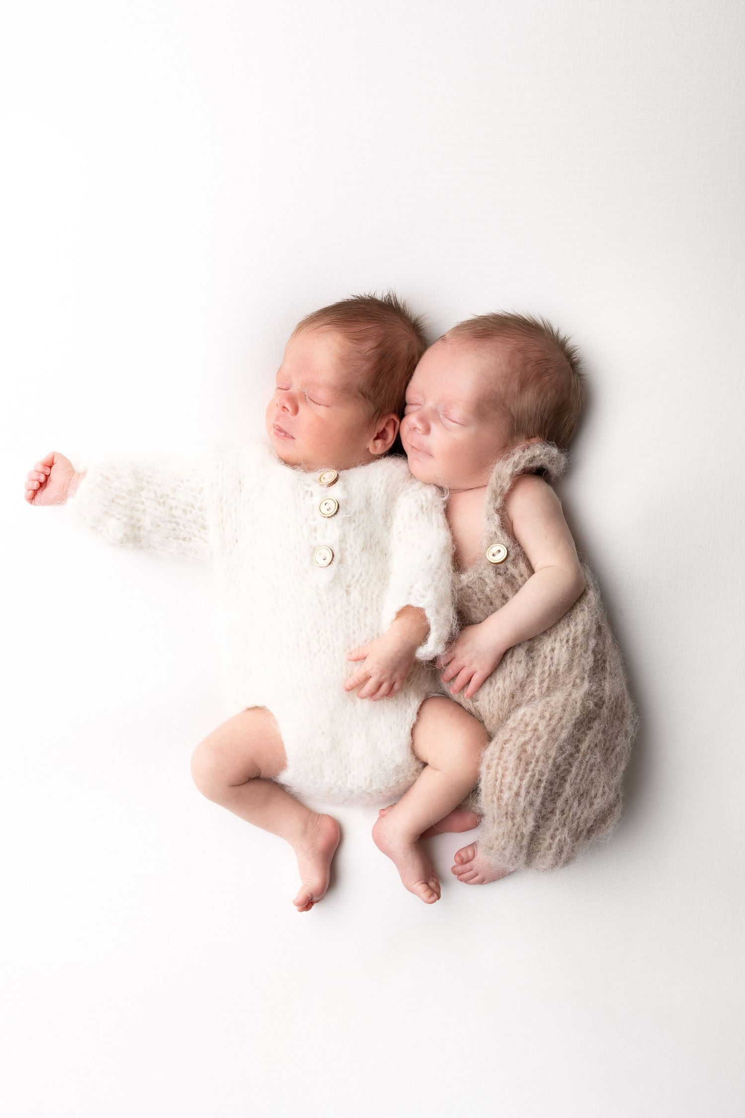 Twin newborn babies sleeping side by side dressed in white and beige knit rompers on white background. photographe naissance chavanoz lyon